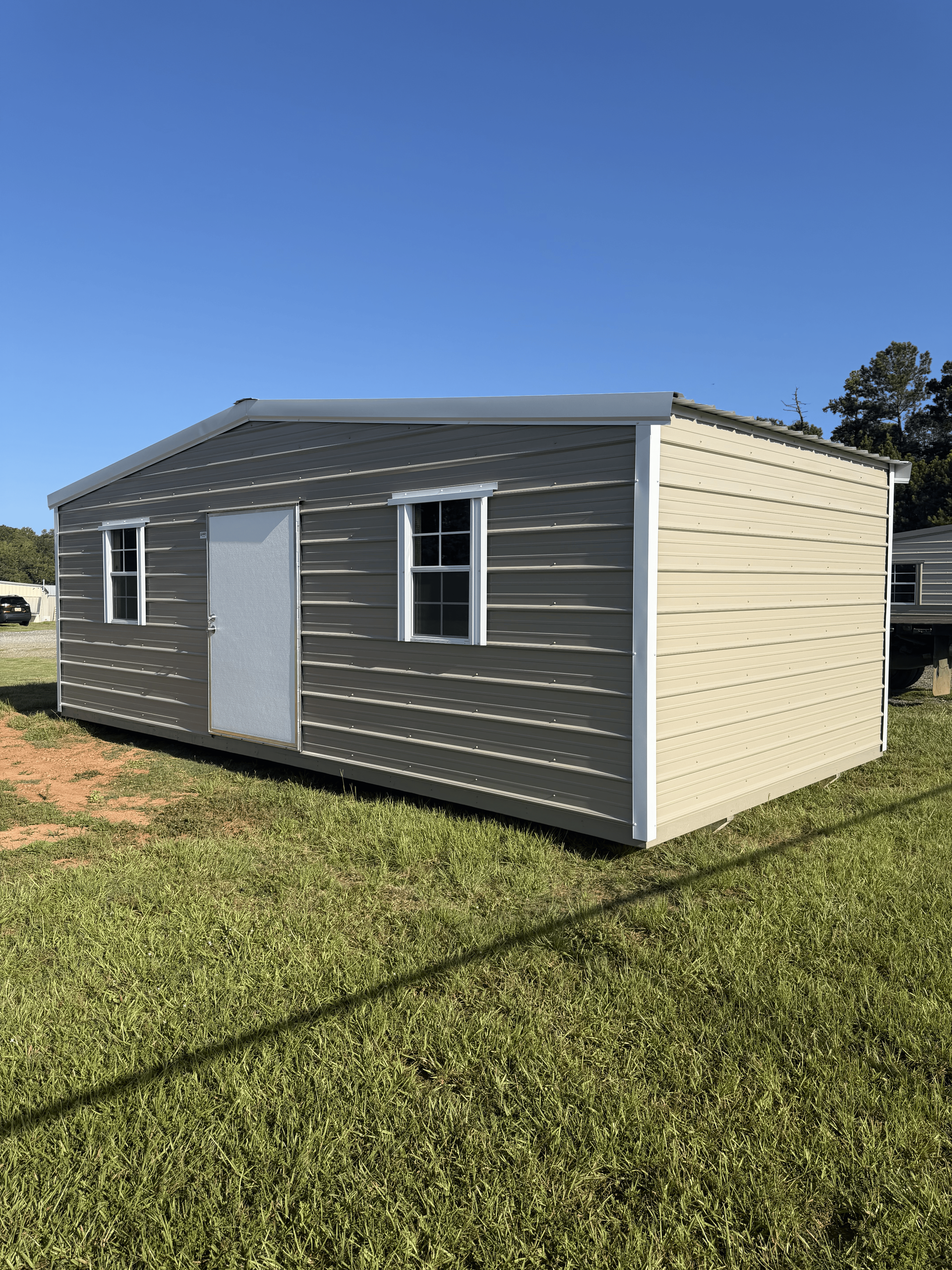 Small gray modular building with white door and windows, sitting on a grassy field under a blue sky