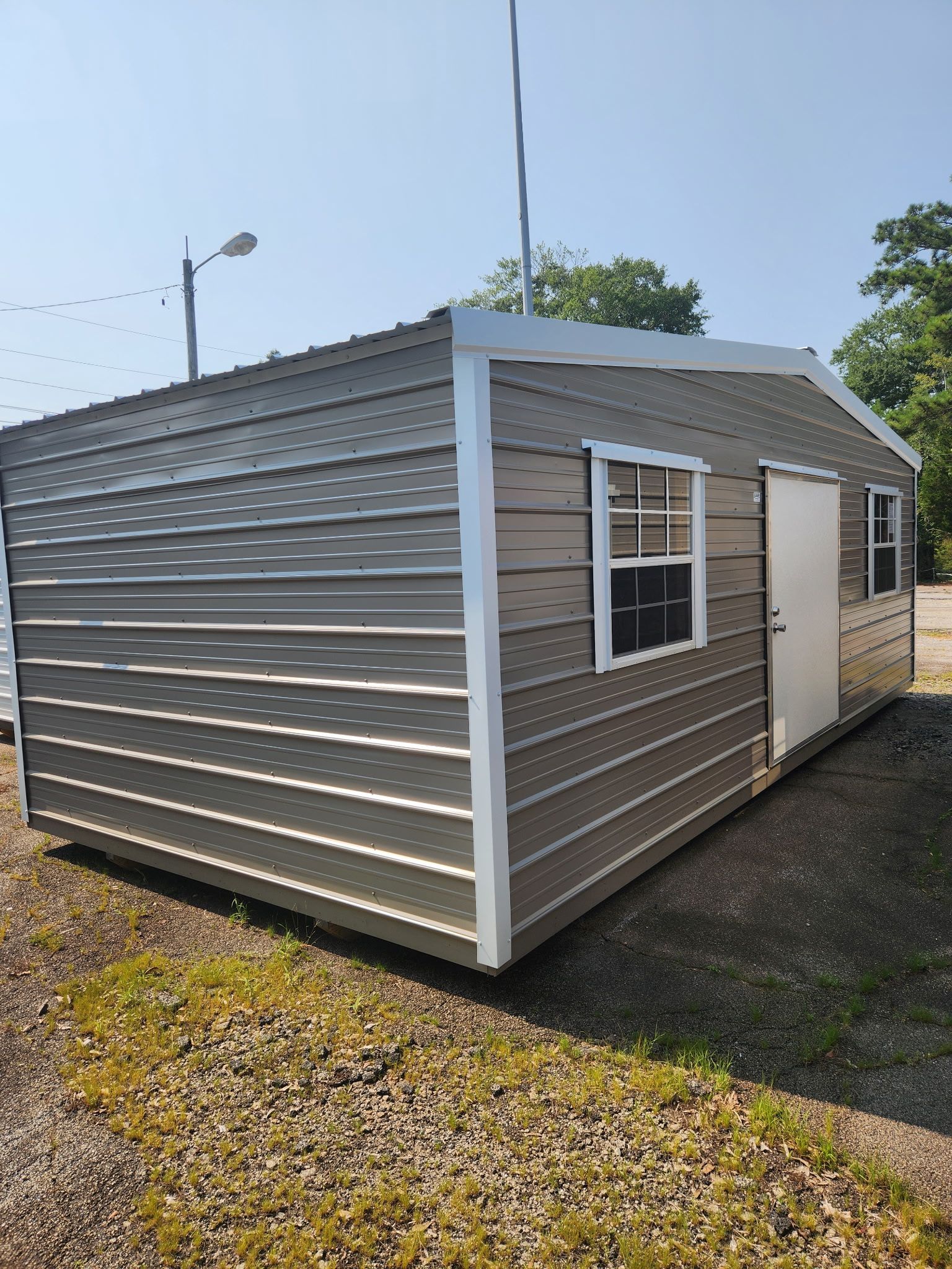 Small tan portable building with white trim and windows, standing on gravel under a clear sky.