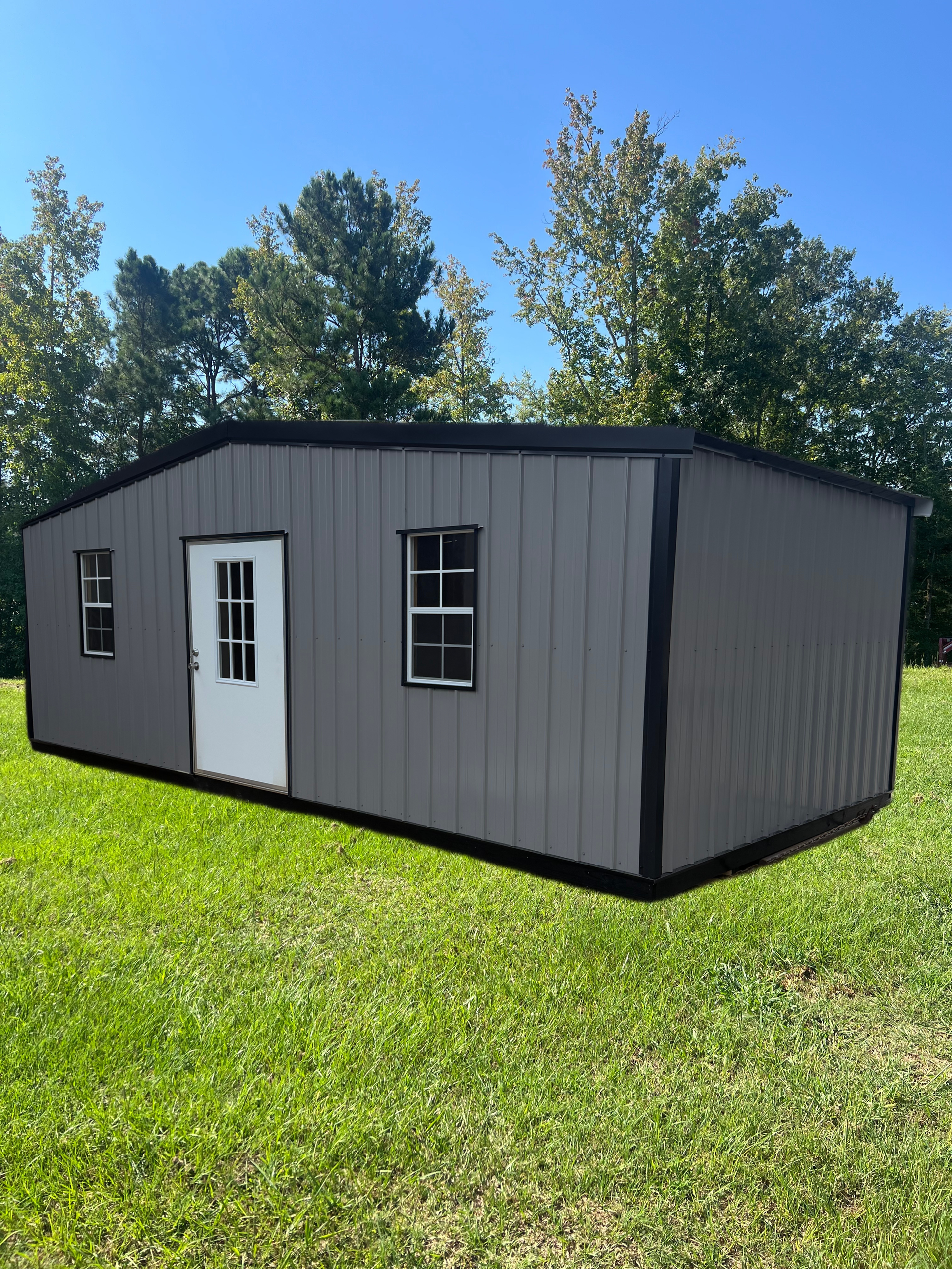Gray modular tiny house with white door and windows on a grassy lawn under trees