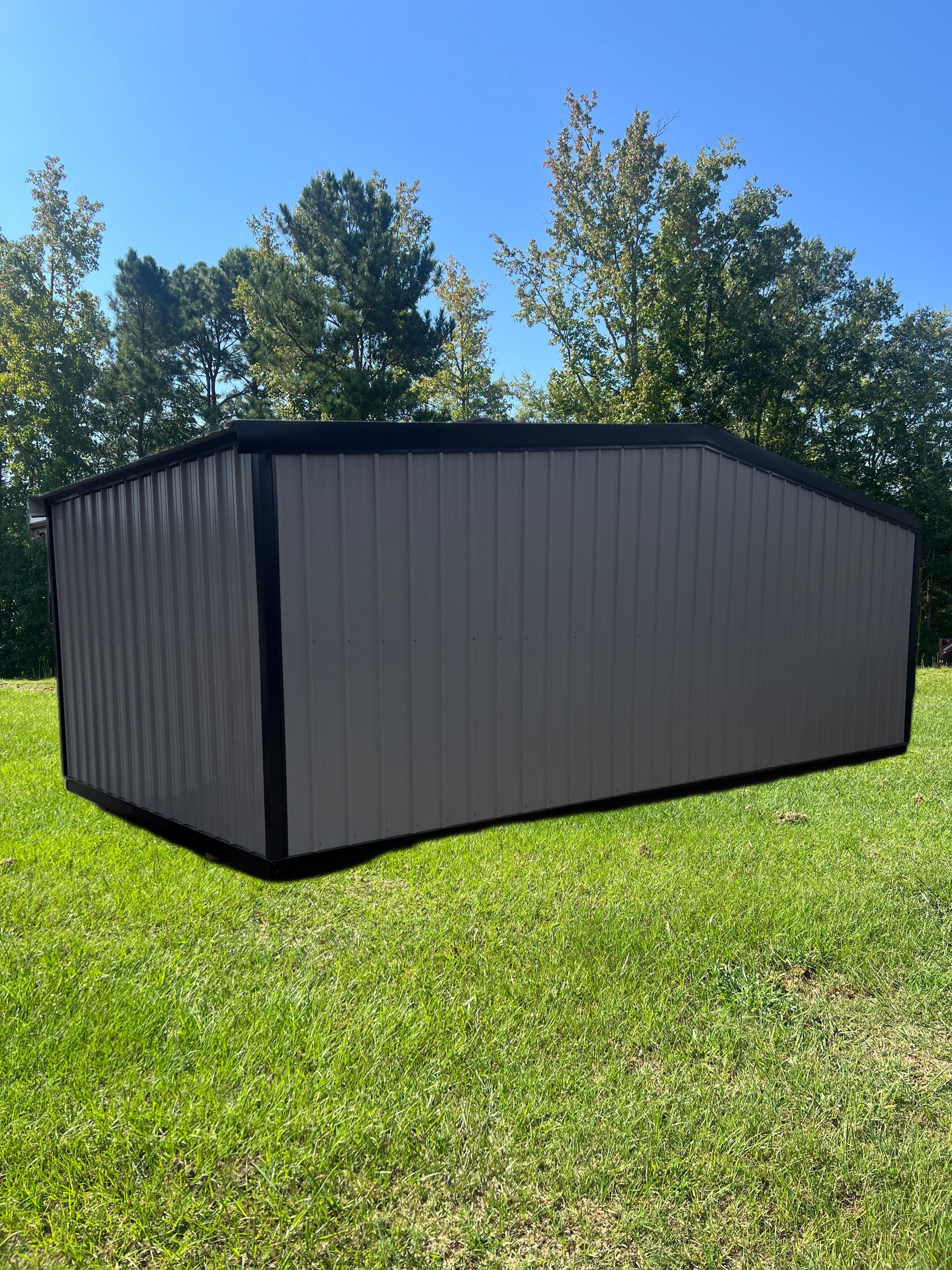 Dark gray metal shed on a grassy lawn with trees and blue sky in the background