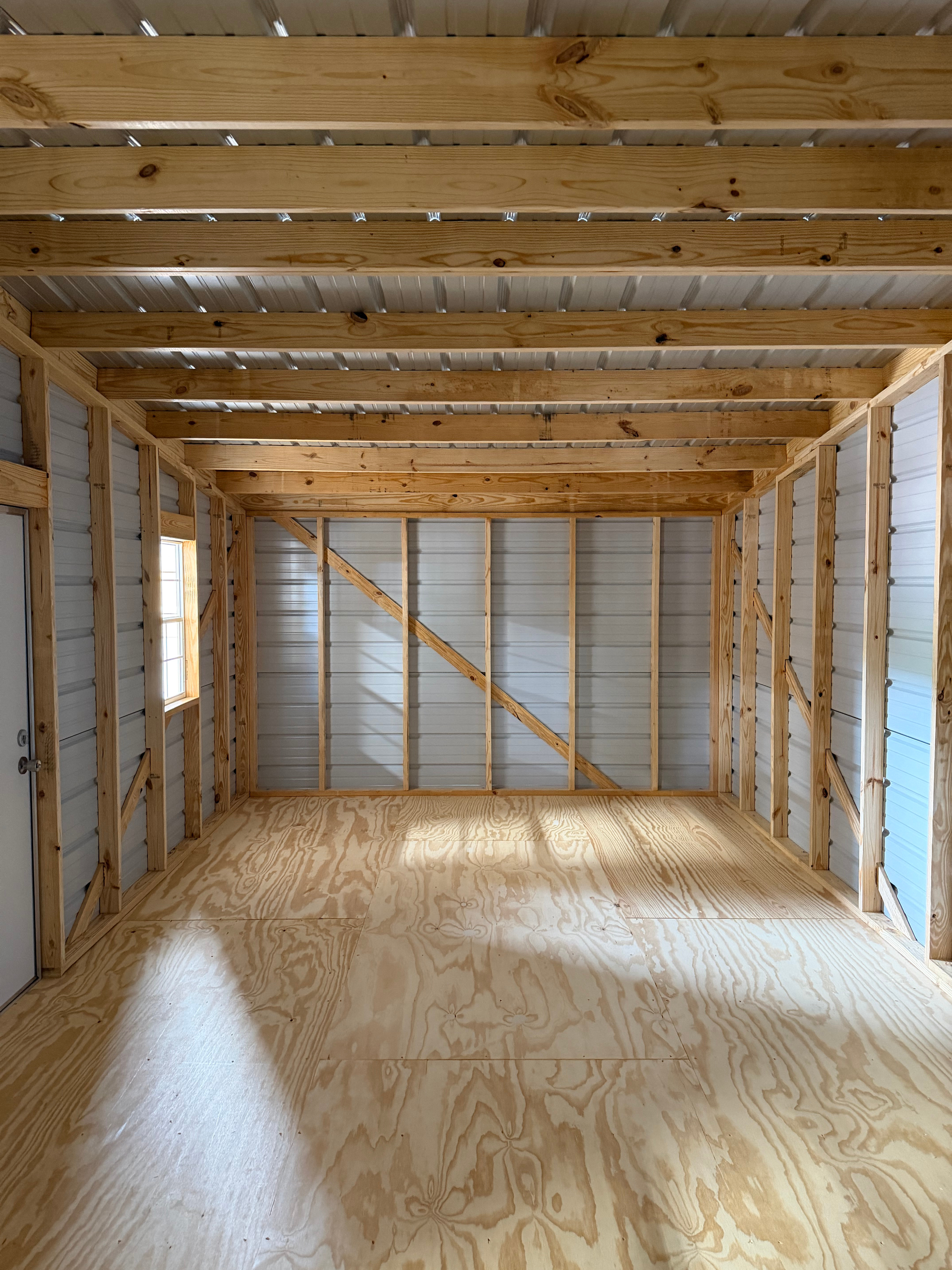 Interior of an unfinished wooden room with exposed studs, beams, and plywood floor and walls
