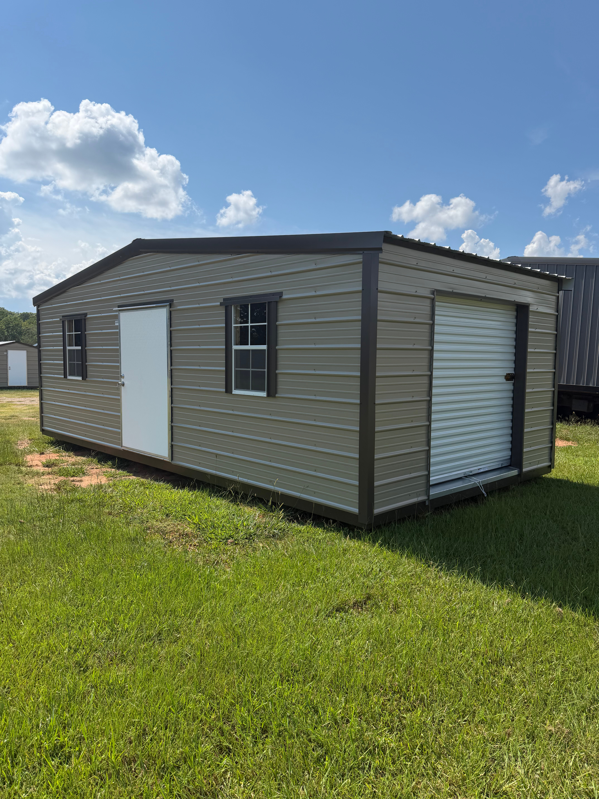 Small gray modular building with white doors and windows on a grassy lot under a blue sky.