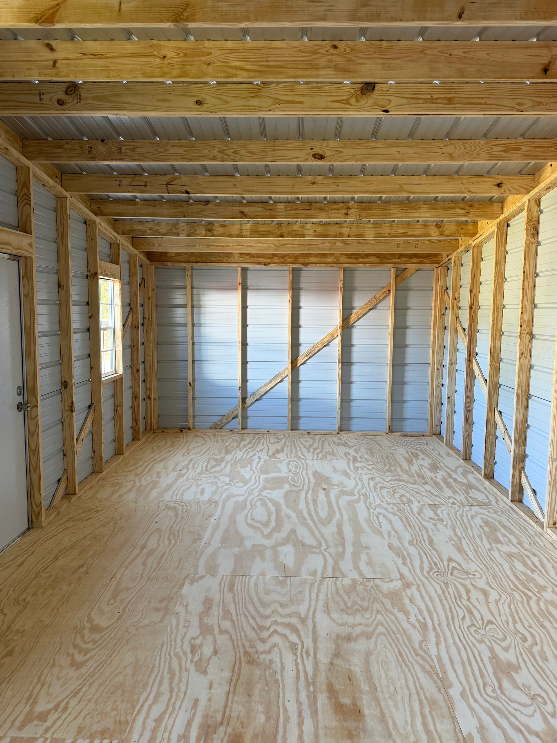 Empty unfinished garage interior with exposed wooden framing and plywood floor