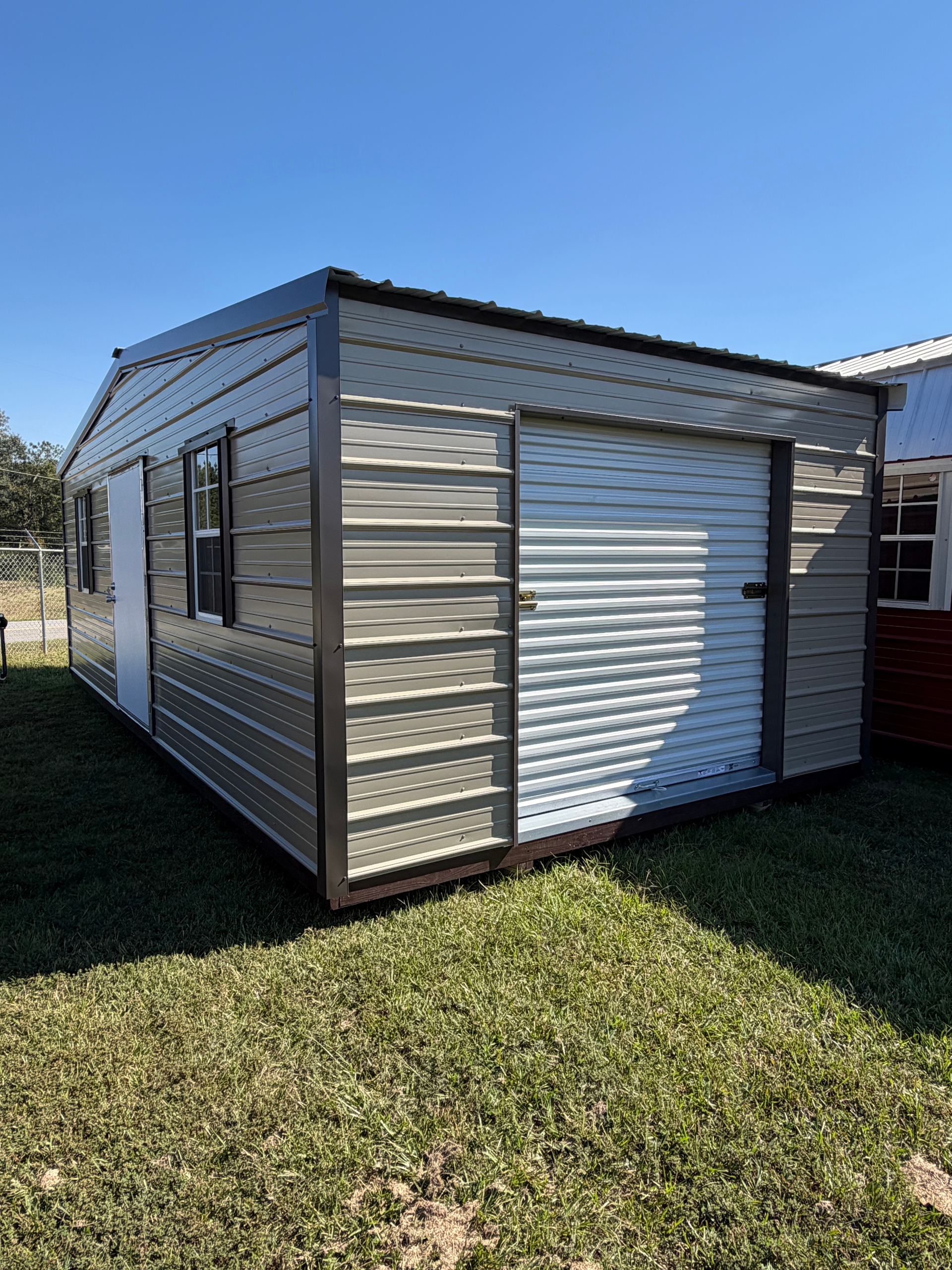 Small gray metal shed with white roller door on grass under a clear blue sky