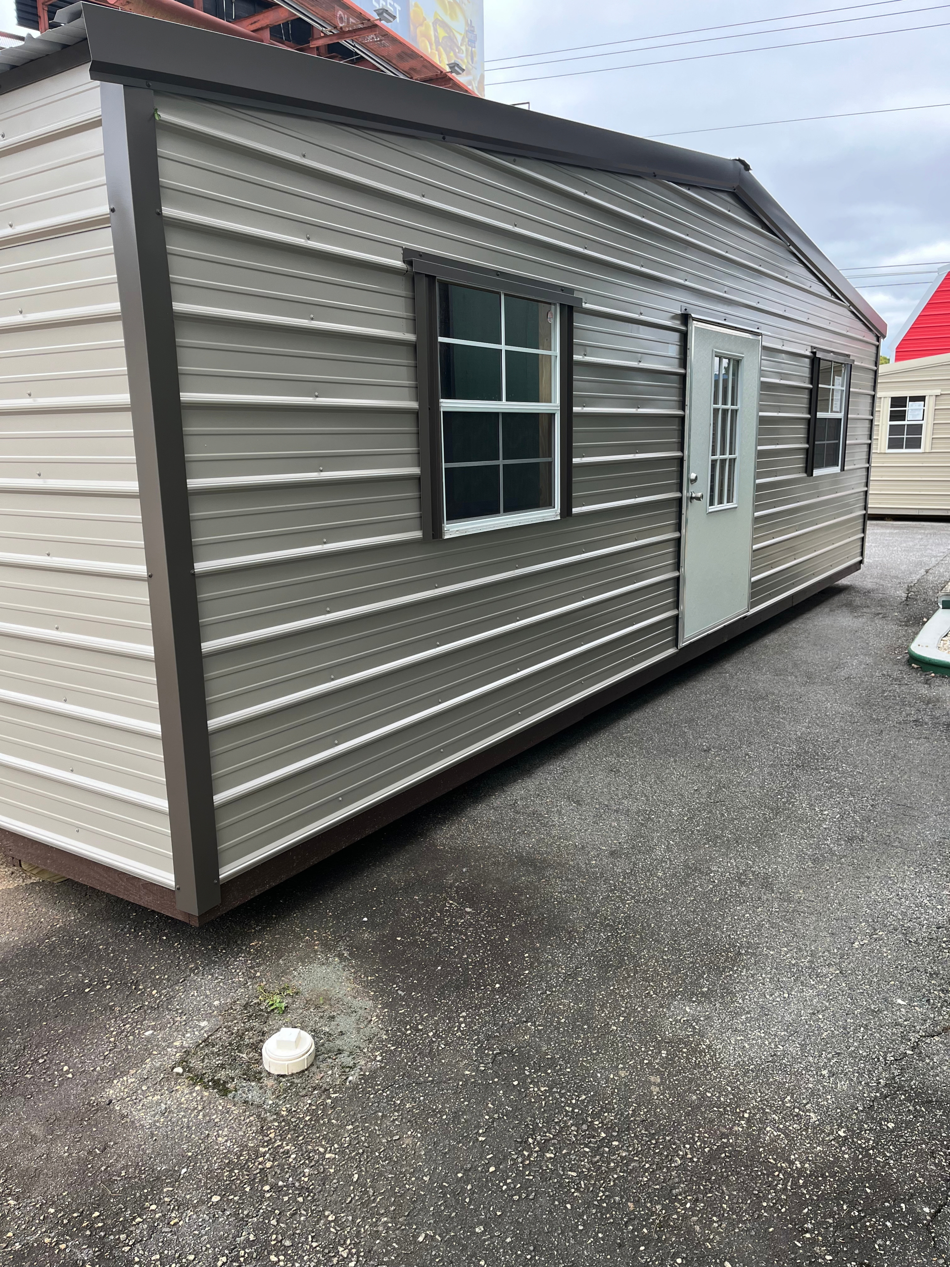 Gray mobile office shed with a window and white door on a gravel lot, under a cloudy sky
