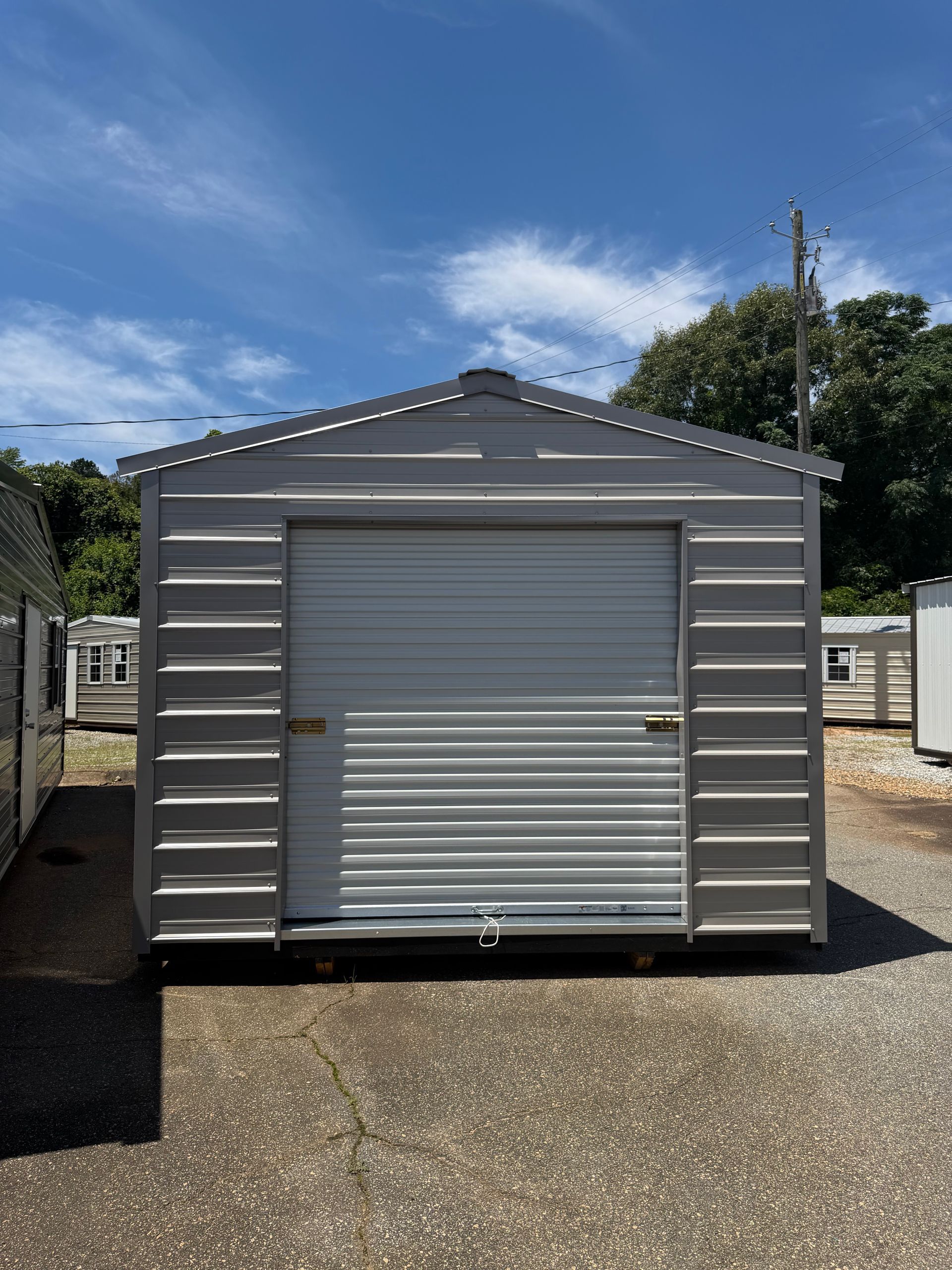 Gray metal shed with a roll-up door under a blue sky on a gravel lot