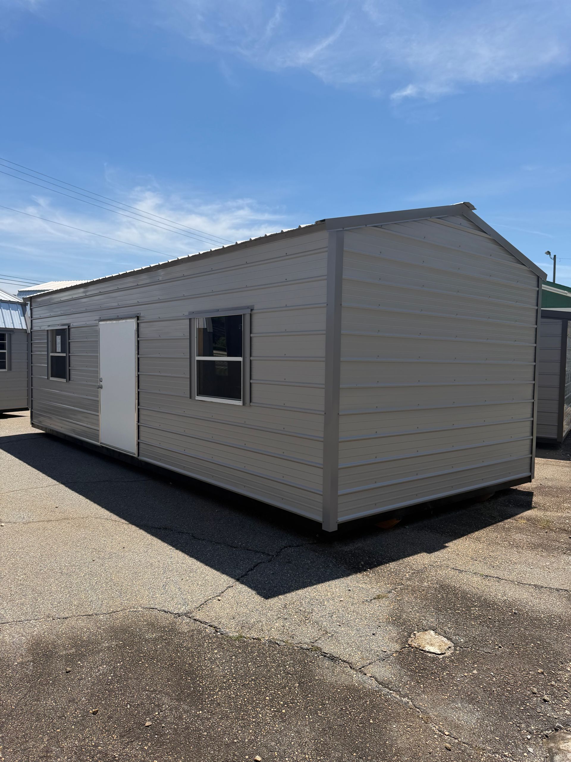 Gray portable building with windows on a gravel lot under a blue sky