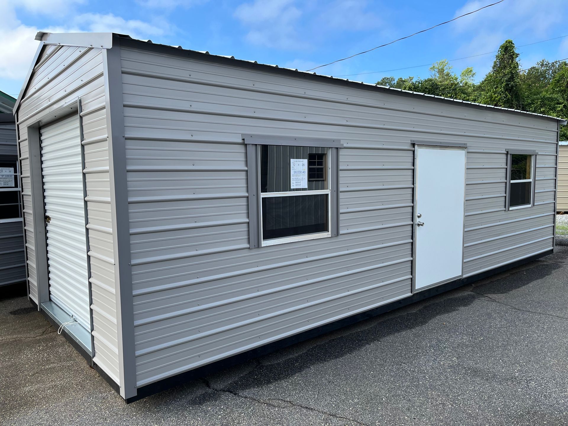 Small gray modular building with a window and white door on a gravel lot under a blue sky
