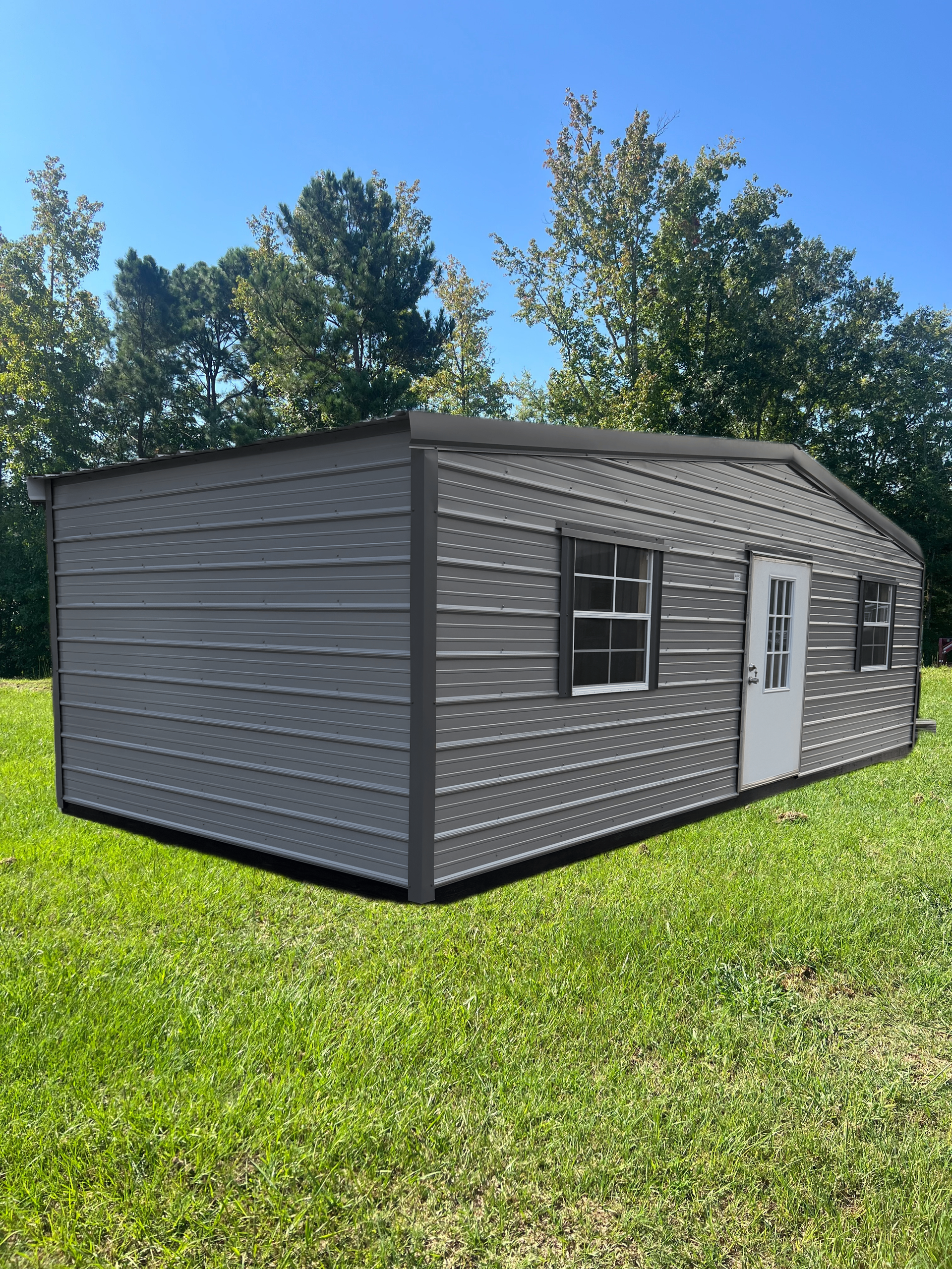 Gray modular shed on a grassy lawn under a blue sky, with trees in the background.