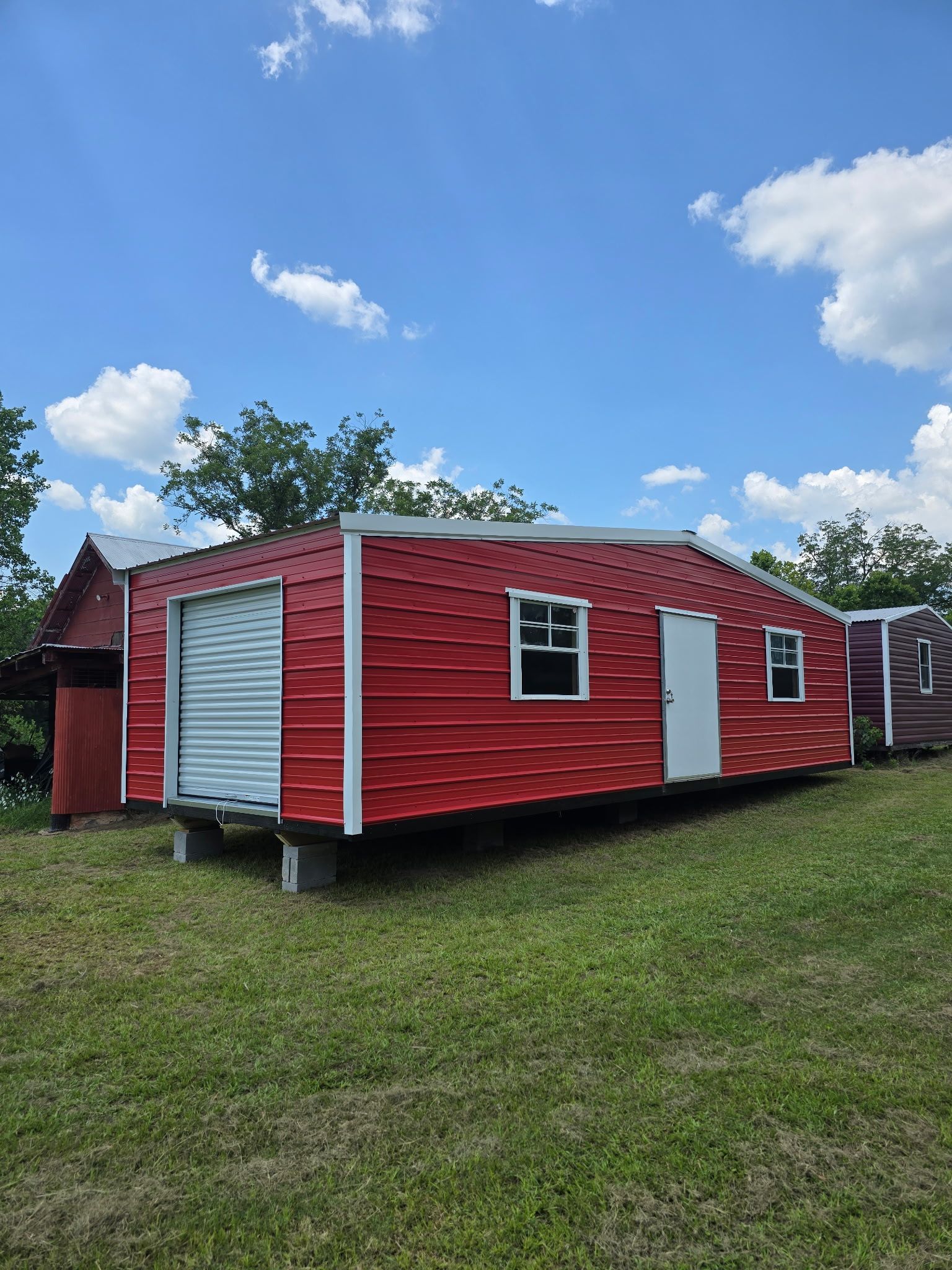 Red mobile home with white trim on grassy lot under a blue sky with clouds