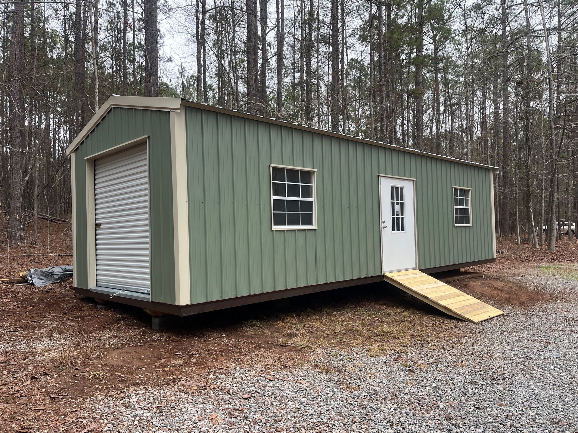 Green metal shed with garage door, windows, and ramp for the door.