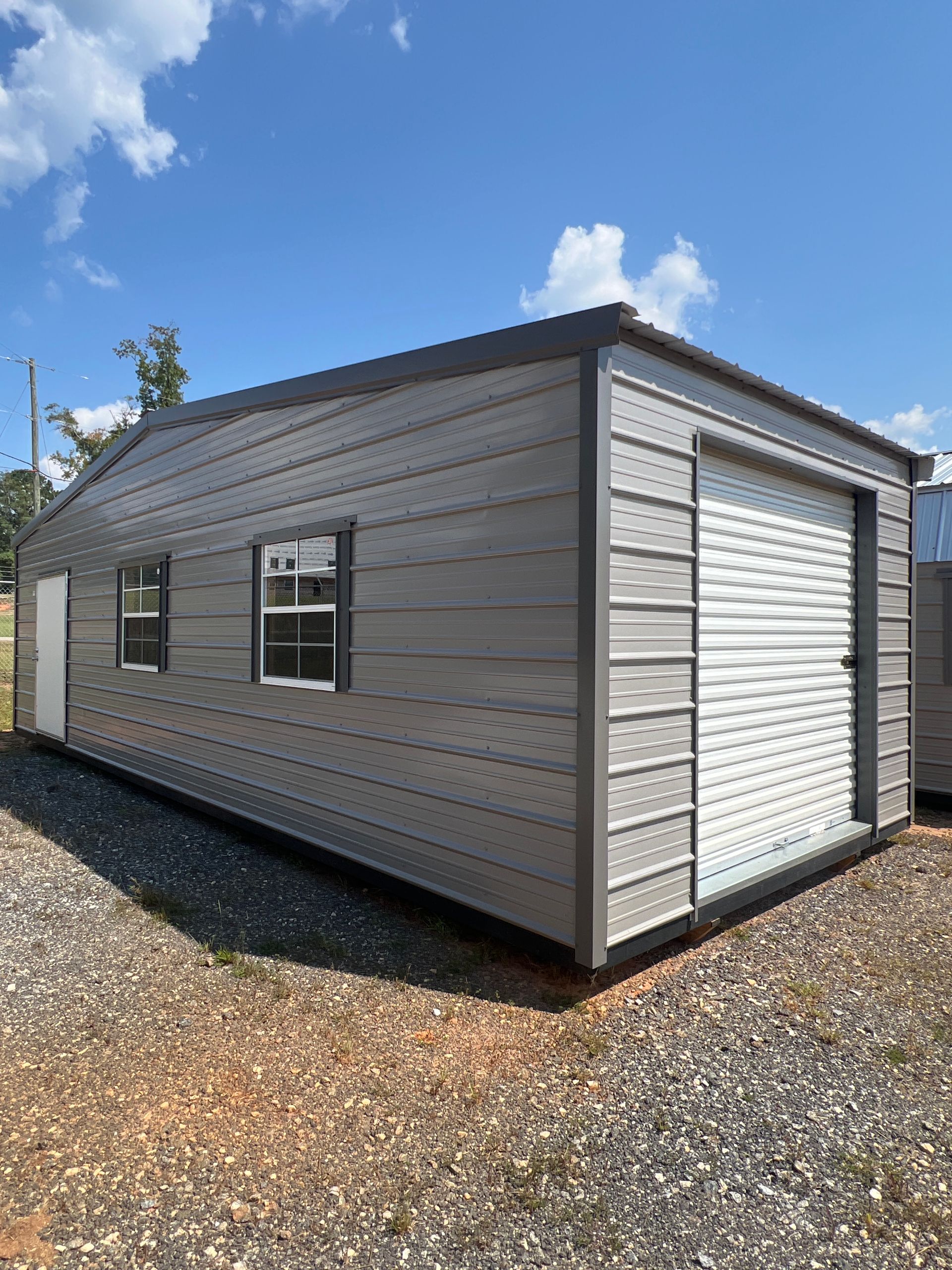 Small beige shed with white doors in a grassy yard under a blue sky