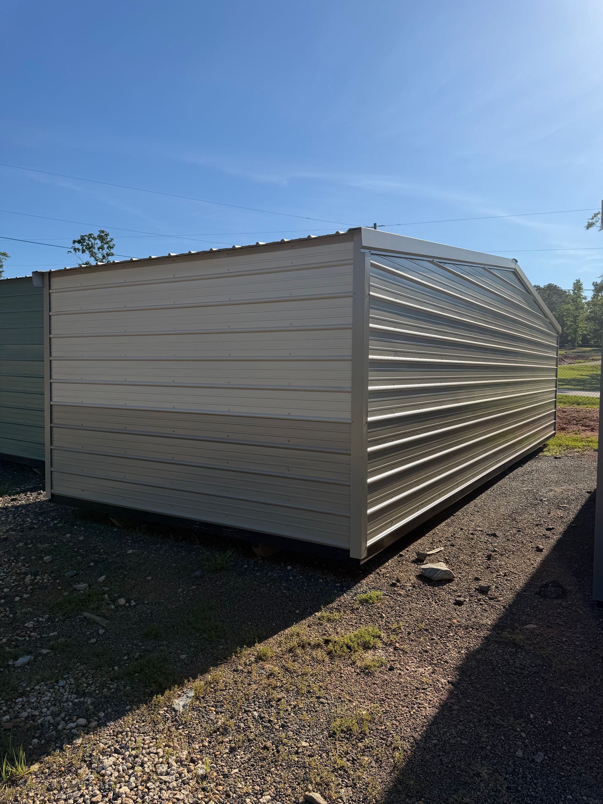 White corrugated metal storage shed on gravel in a sunny outdoor yard