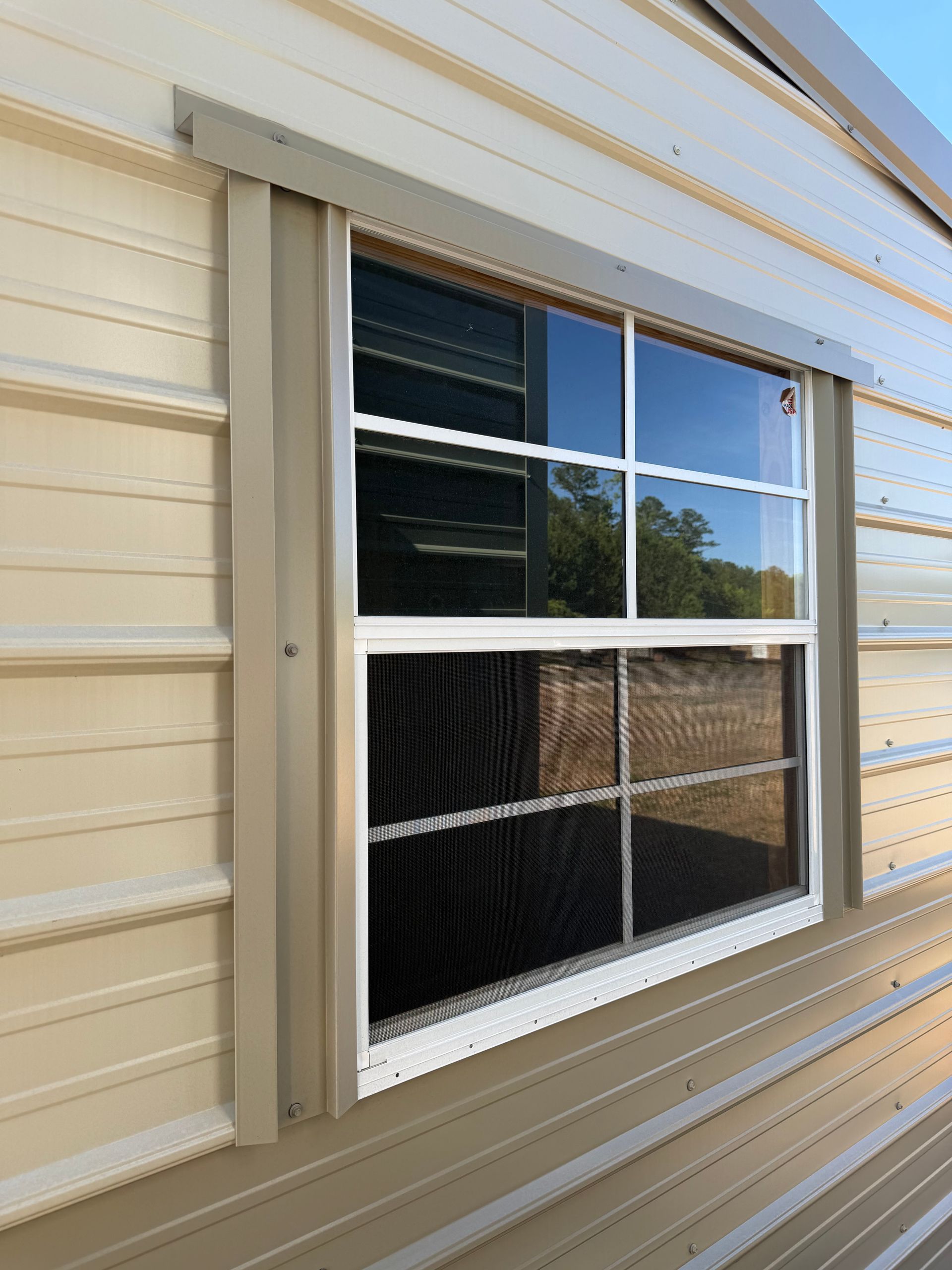White-framed window on a beige siding wall with reflections of trees and sky