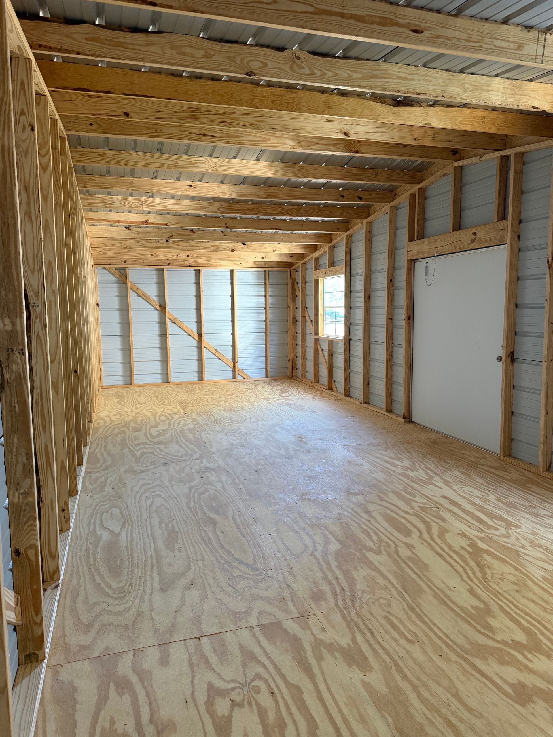 Unfinished wooden room with exposed beams, plywood floor, and insulation in the walls.