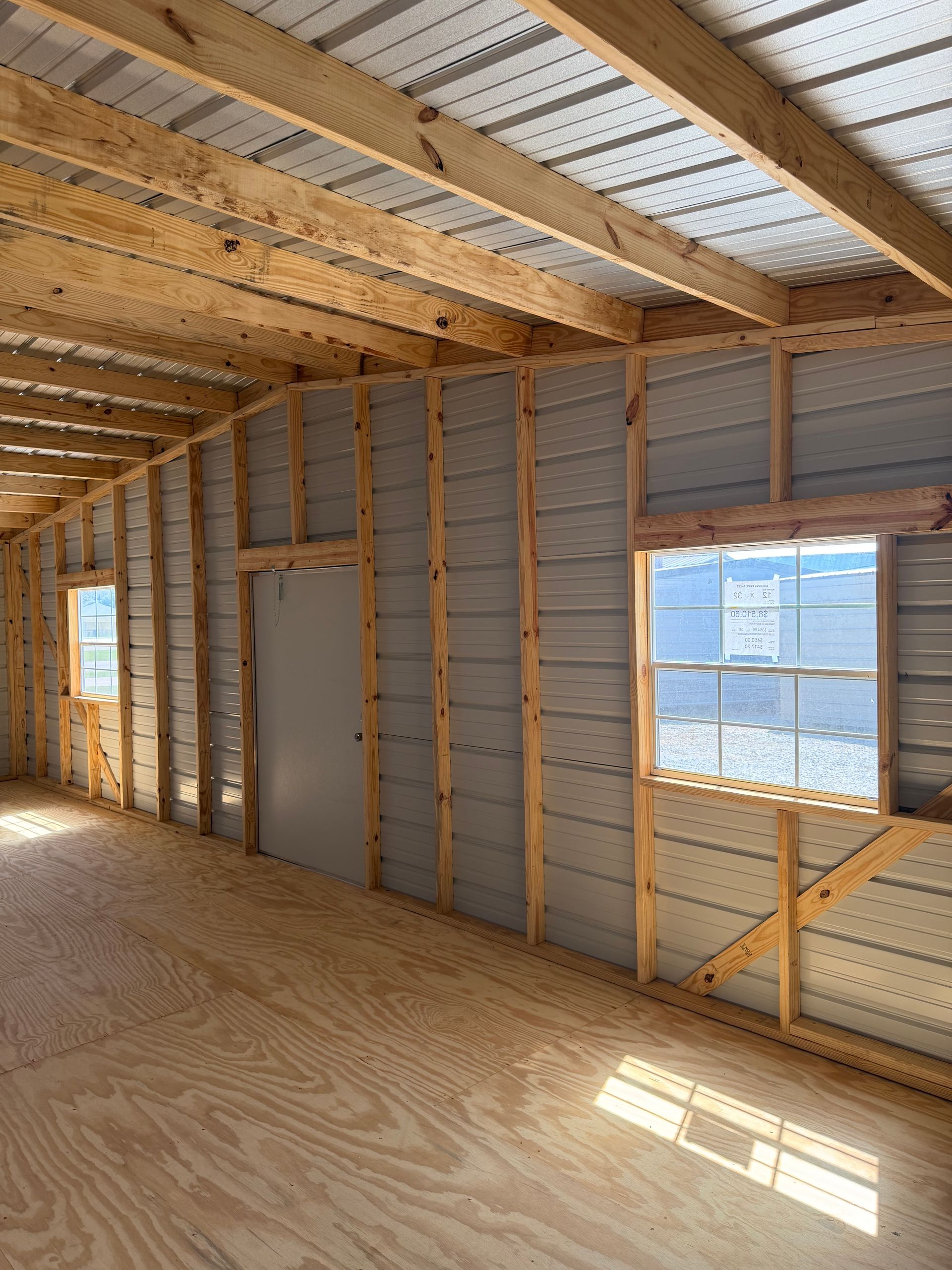 Interior of an unfinished house with exposed studs, plywood flooring, and sunlight through windows.