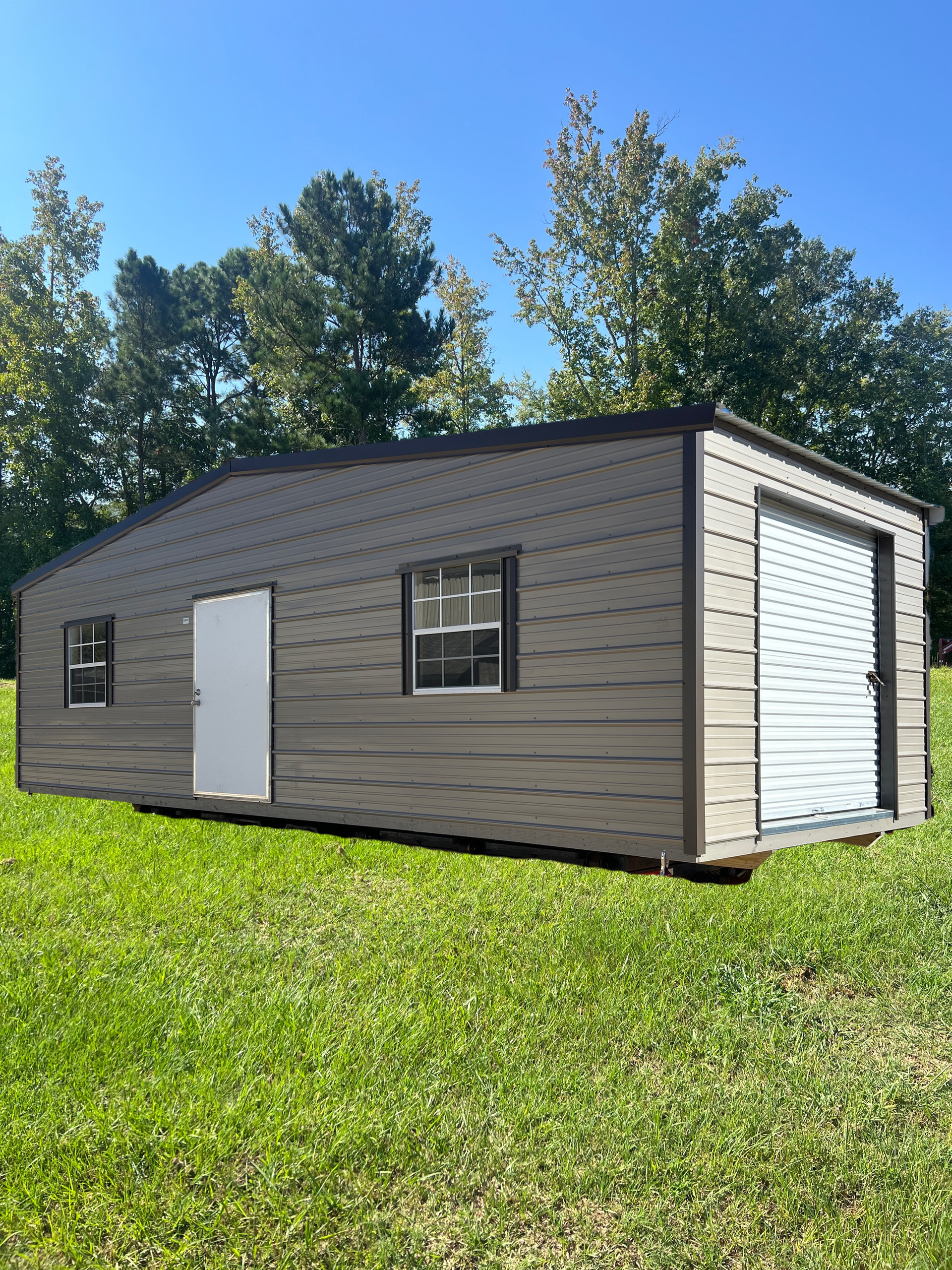 Small gray metal shed with white doors and windows on a grassy lawn under a blue sky