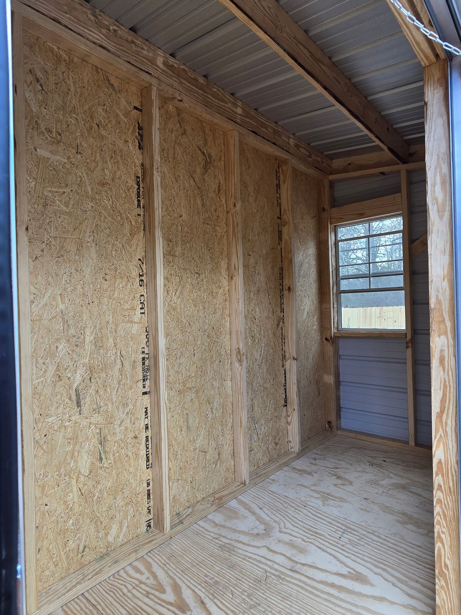 Interior of a small room with wood frame walls, particle board, and a corrugated metal roof.