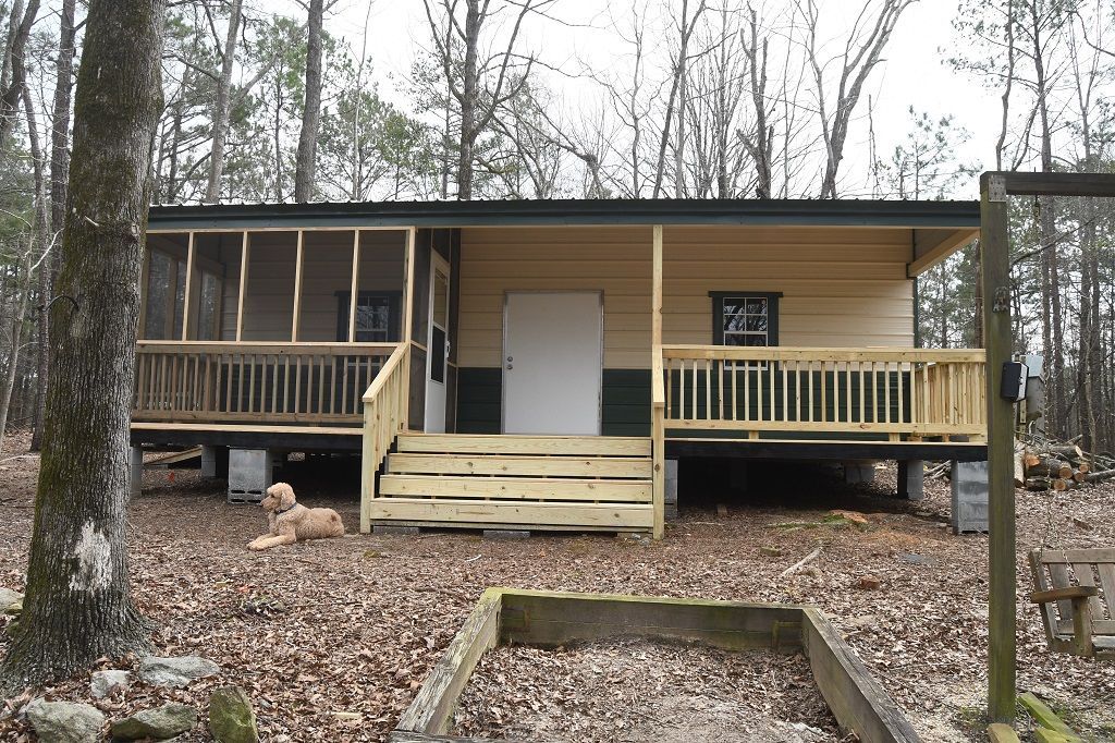 Cabin with screened porch, wooden deck and stairs, dog lying in front. Forest setting.