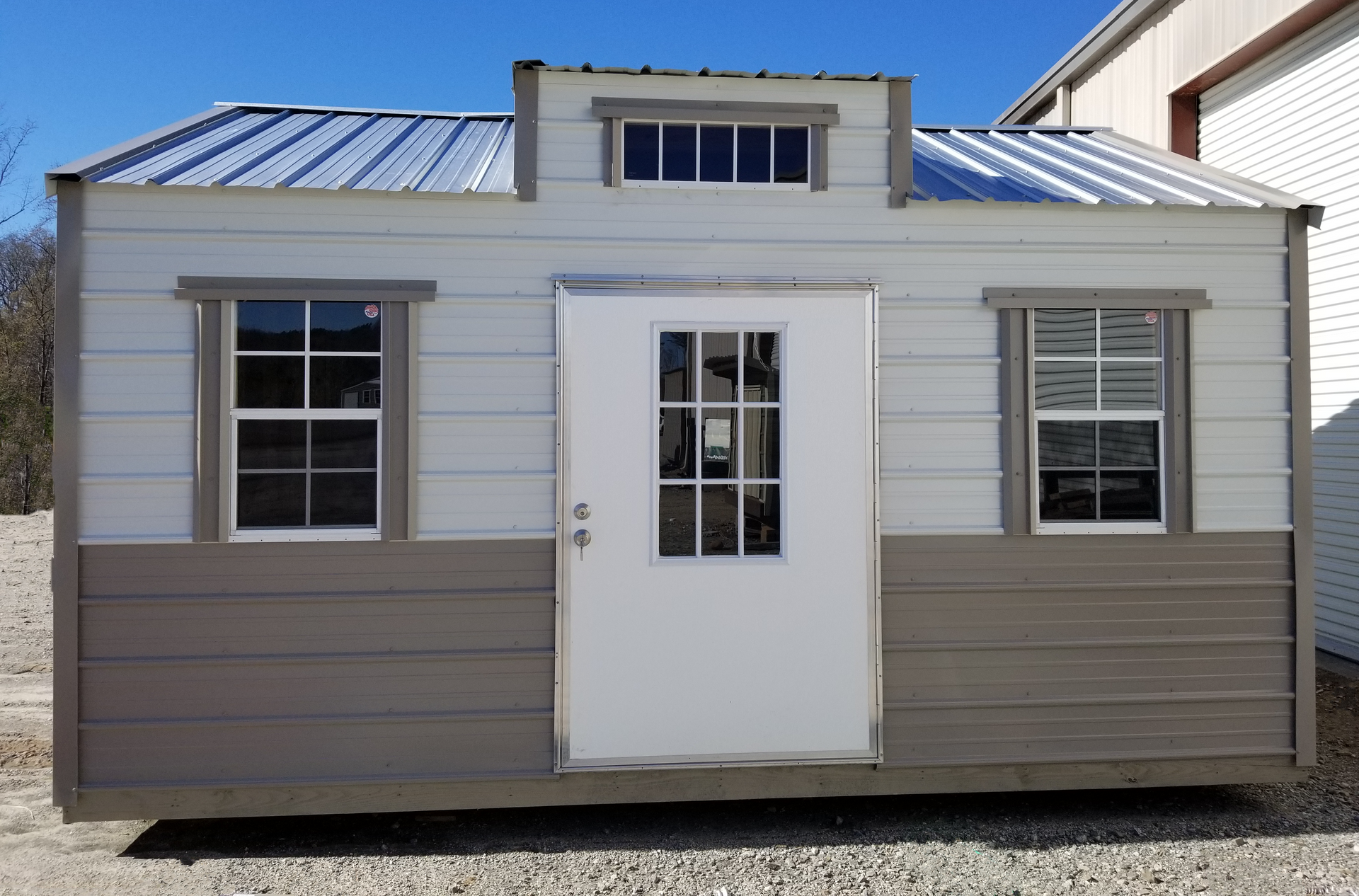 Small beige cabin with white door and windows, shown front view against a blue sky.