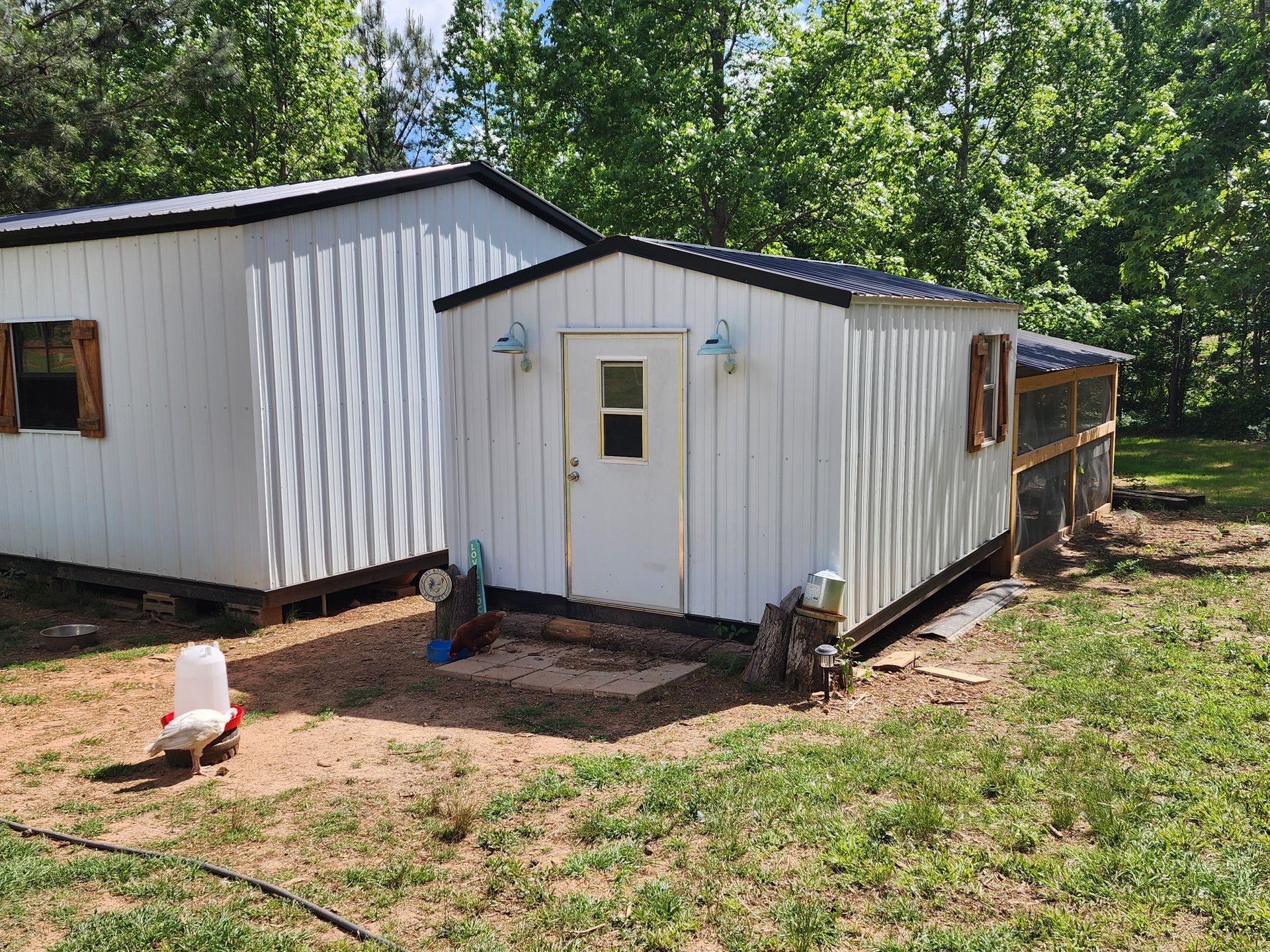 A white shed is sitting in the middle of a grassy field.
