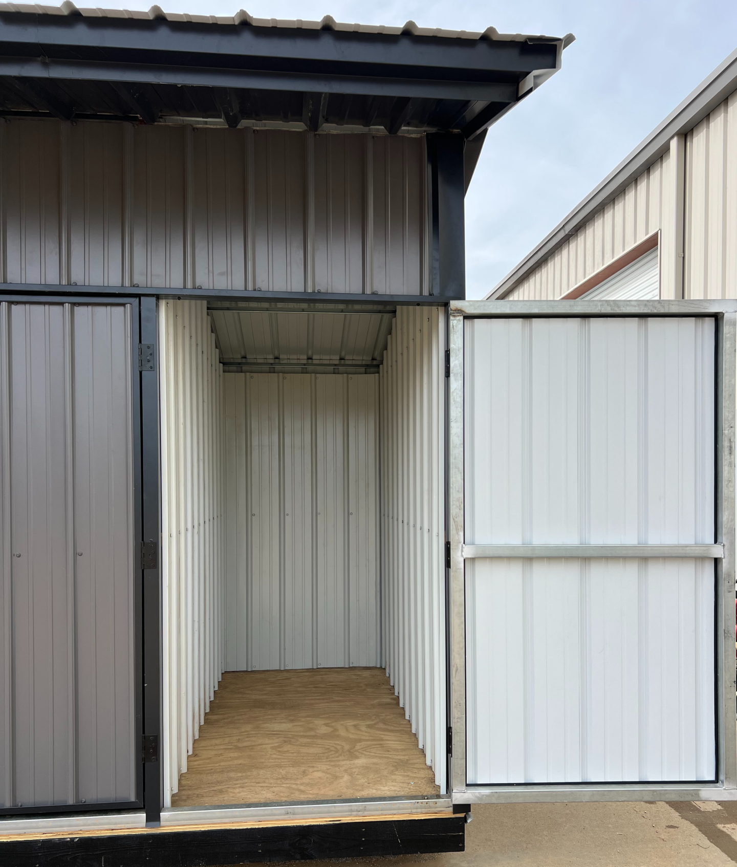 Open metal storage unit with corrugated white walls and a gray door.