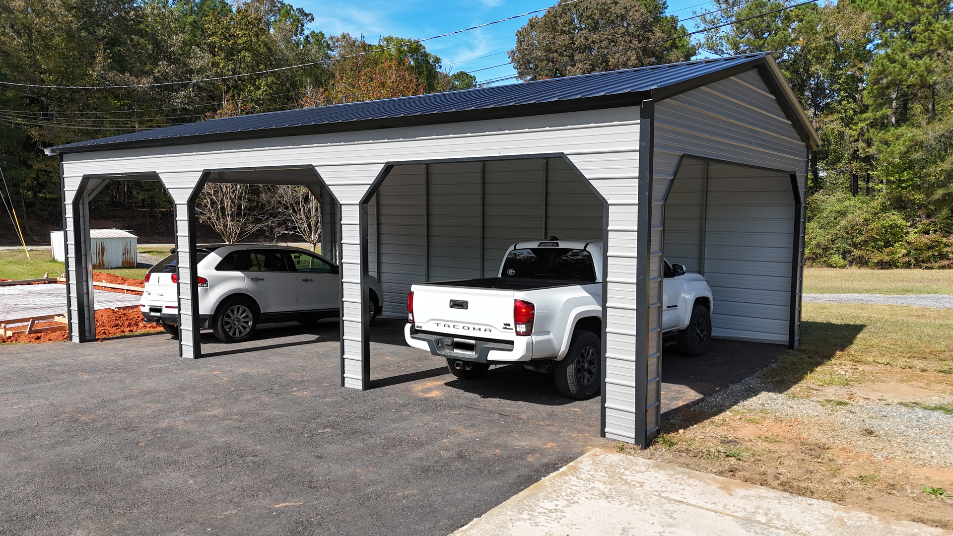 Metal carport with three bays, housing a white SUV and pickup truck, in a rural setting.