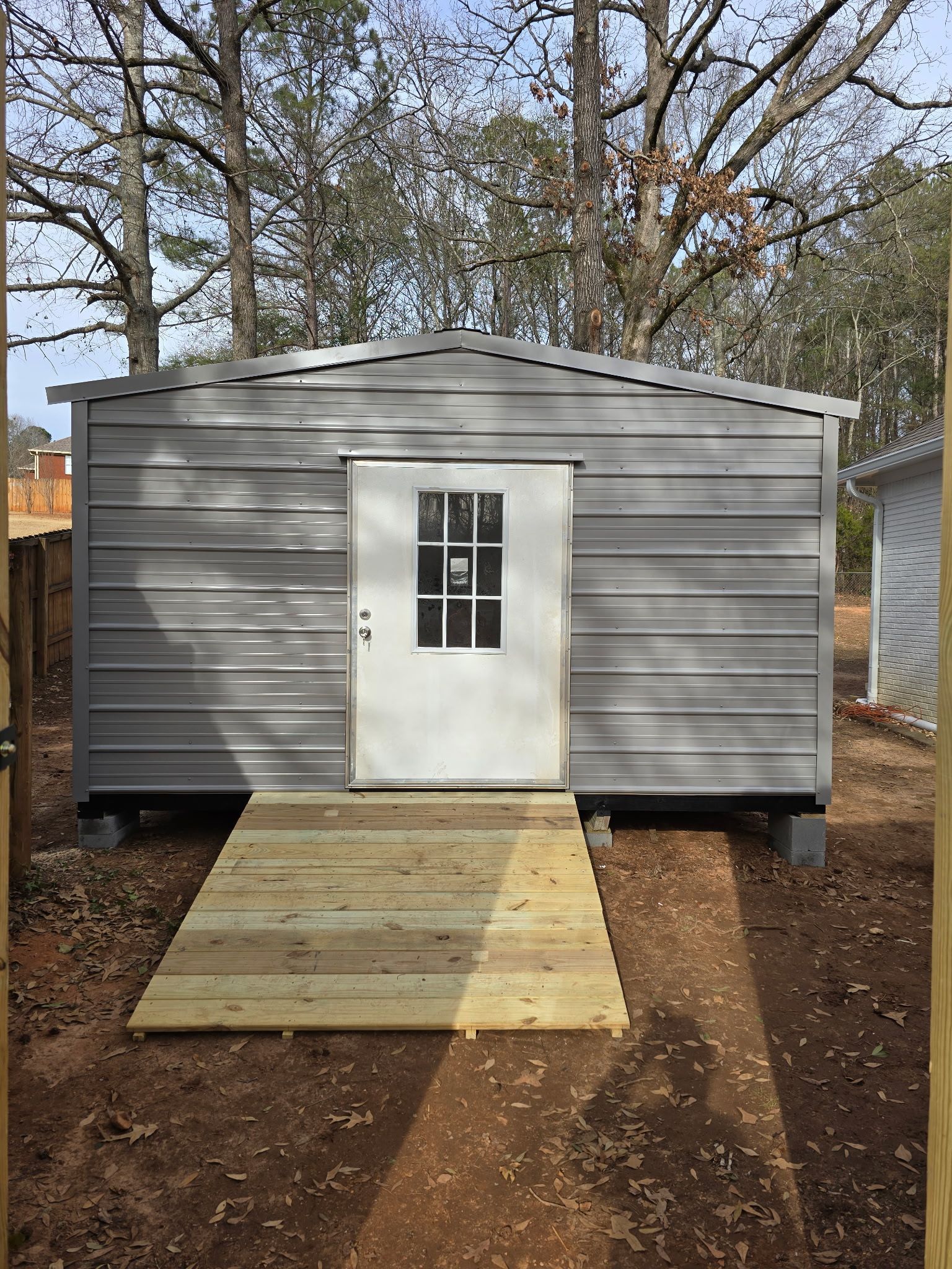 Gray metal shed with a white door and wooden ramp.