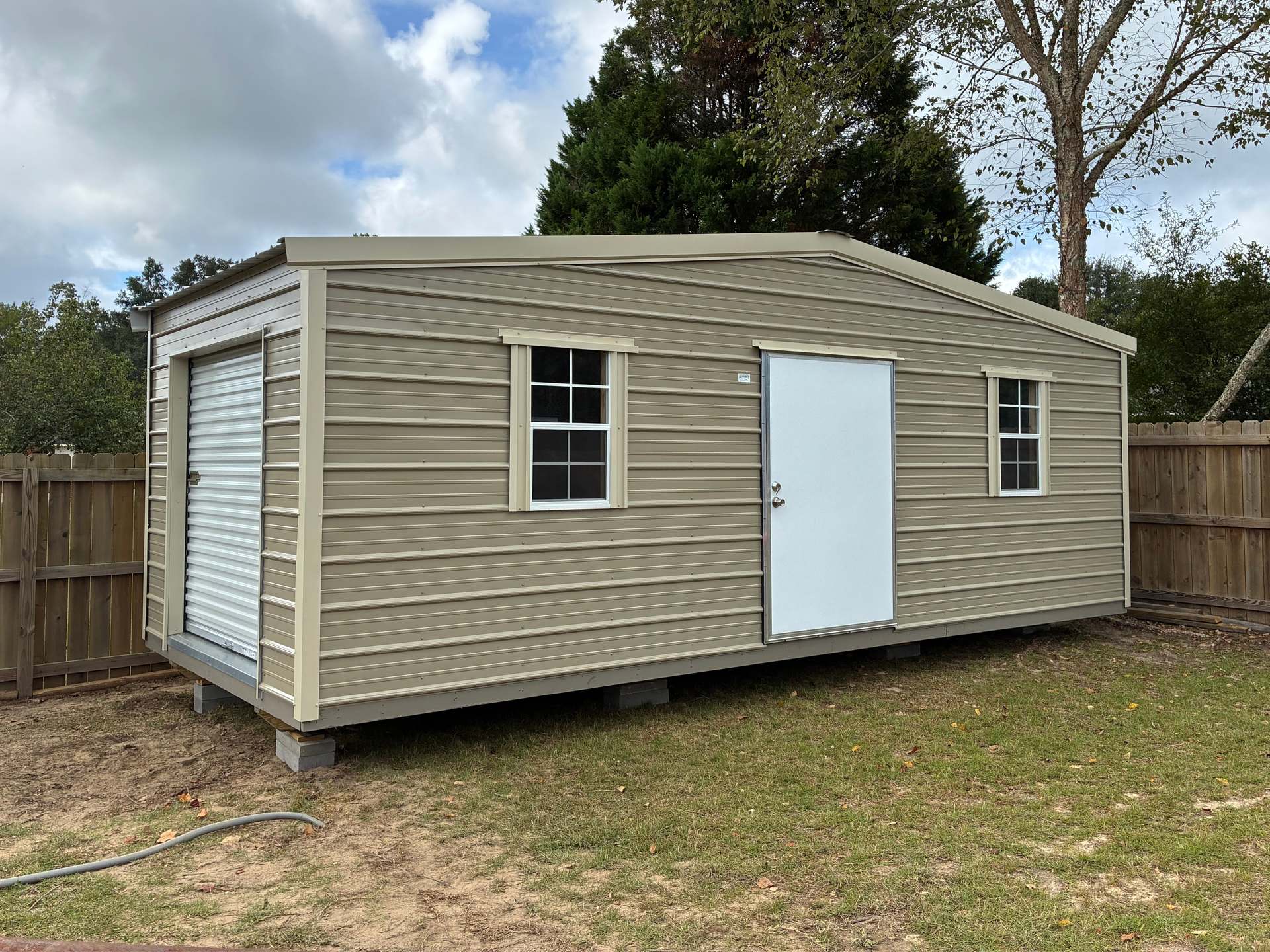 Beige portable storage shed with white door and windows in a grassy yard