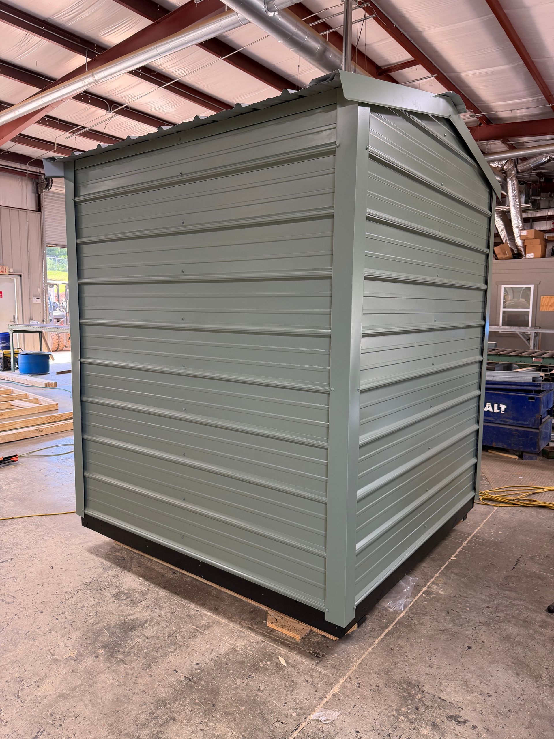 Gray metal storage shed in a warehouse with a ribbed exterior and slanted roof.