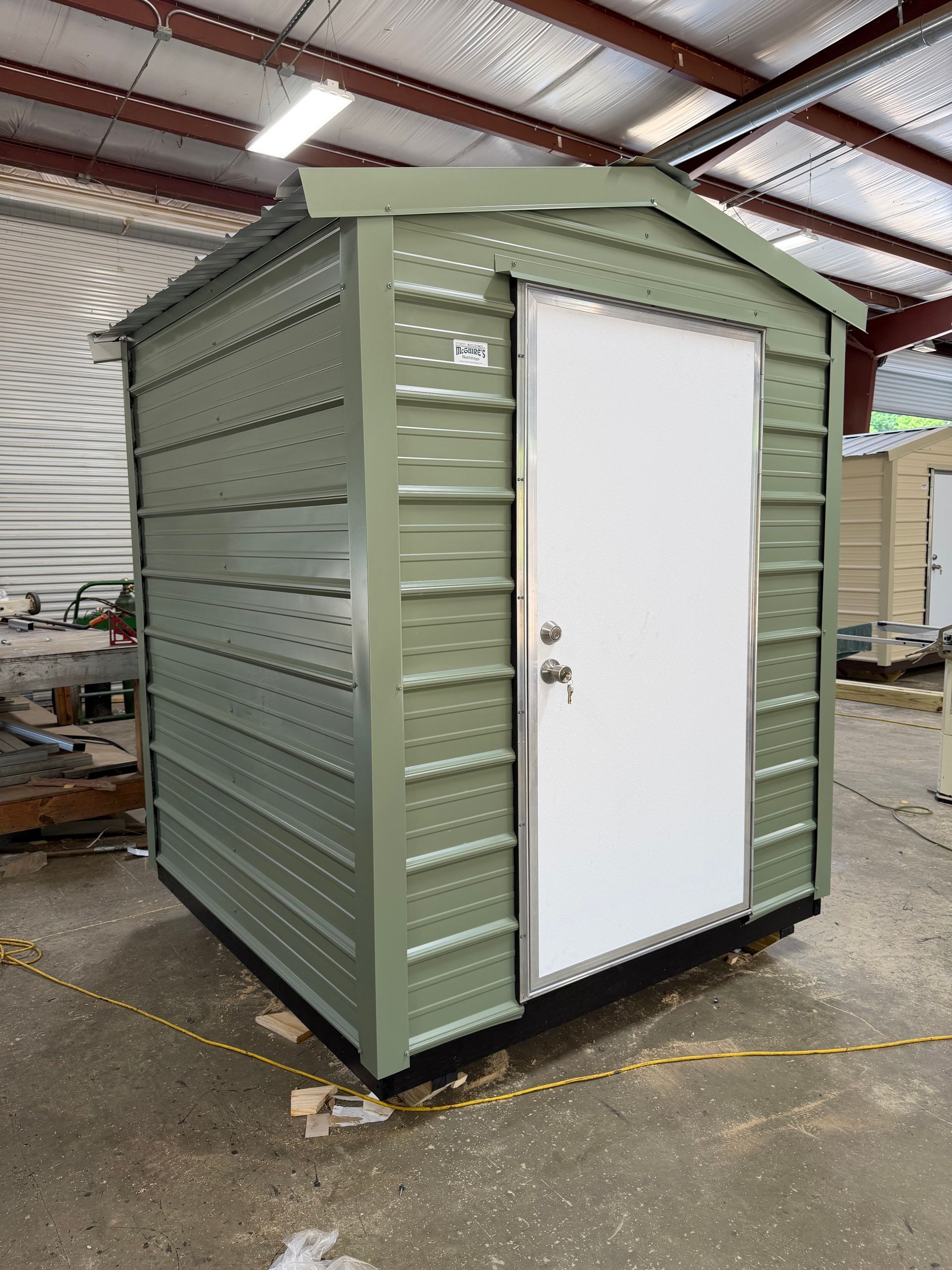 Small green metal shed with a white door inside a warehouse or workshop.
