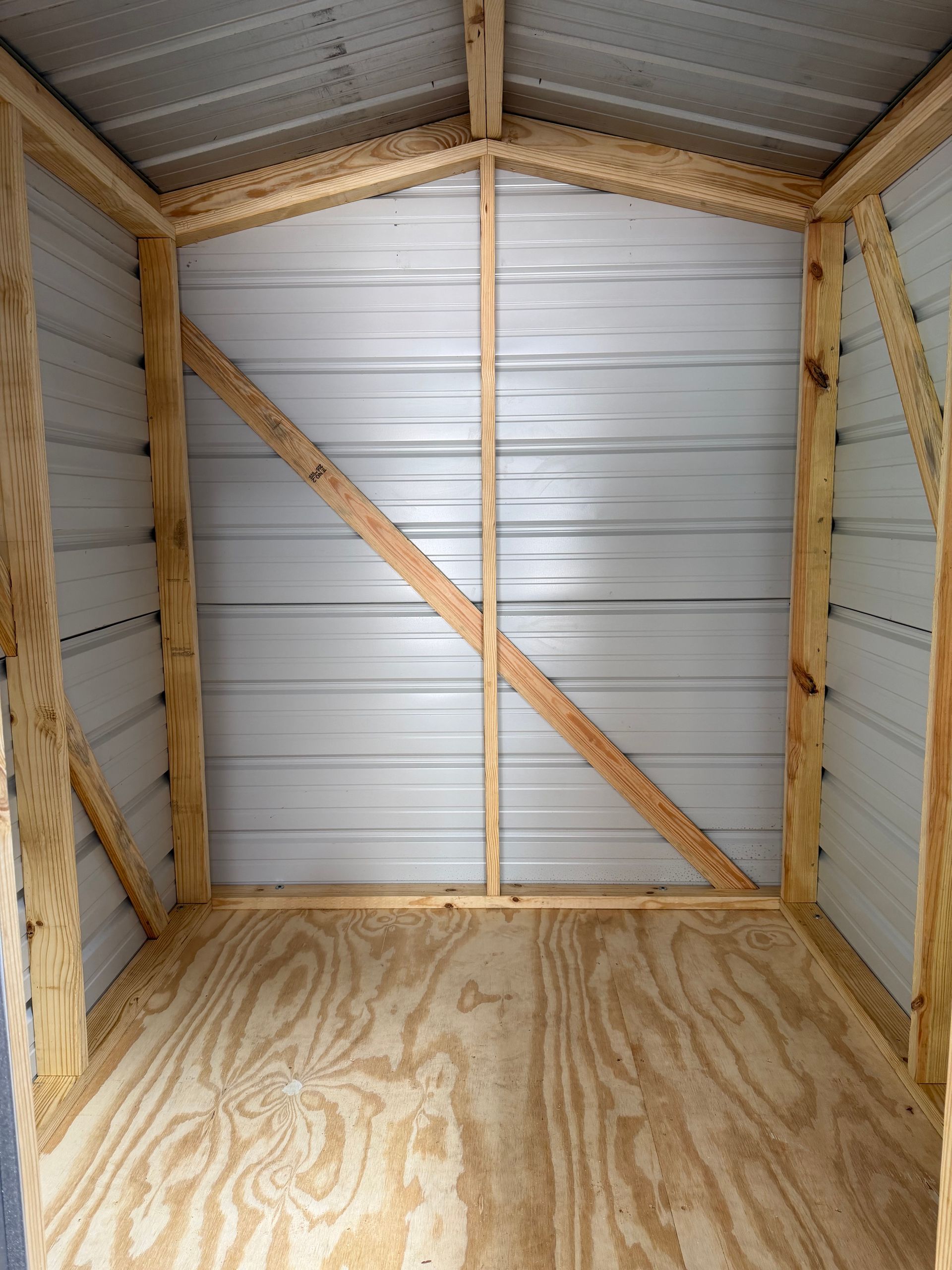 Empty wooden storage shed with plywood floor and metal roof, viewed from the open front.