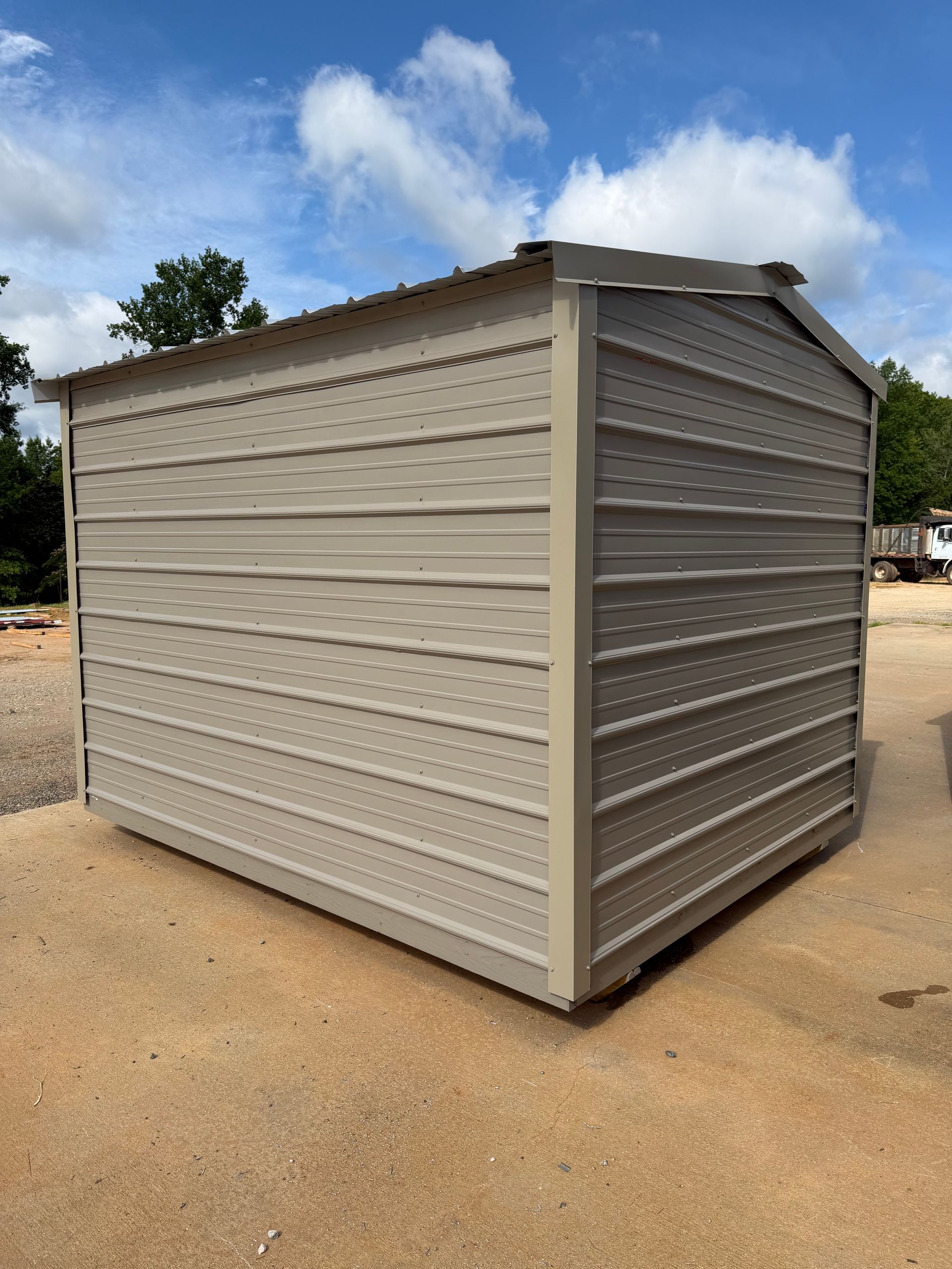 Gray metal storage shed on a dirt lot under a blue sky with clouds