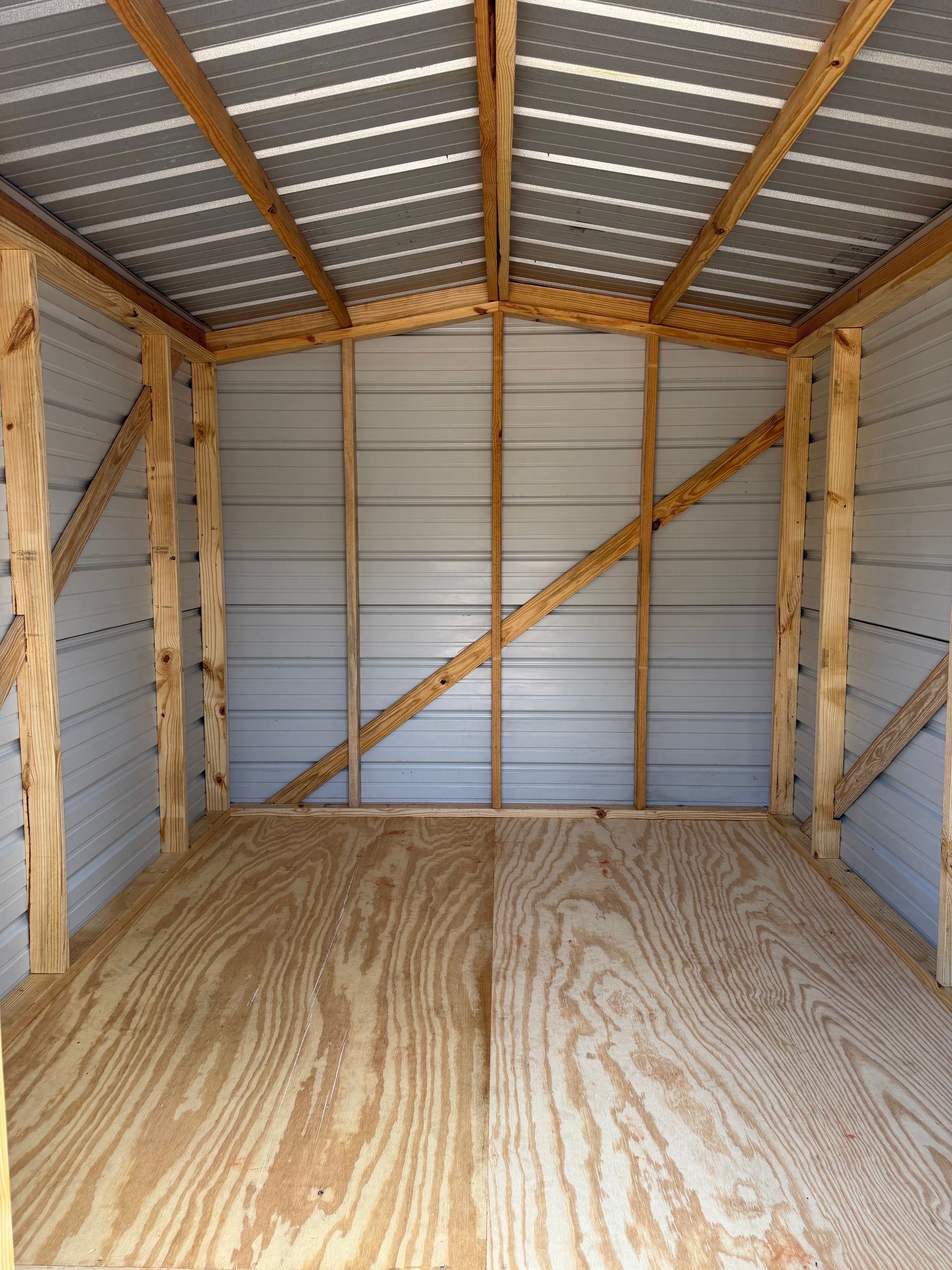 Empty wooden storage shed interior with plywood floor and corrugated metal walls and roof braces