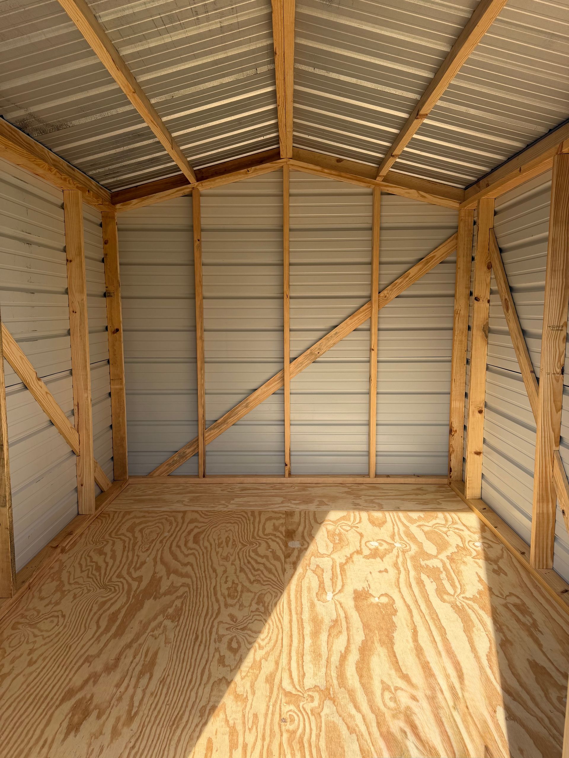 Empty wooden storage shed interior with plywood floor and corrugated metal roof and walls