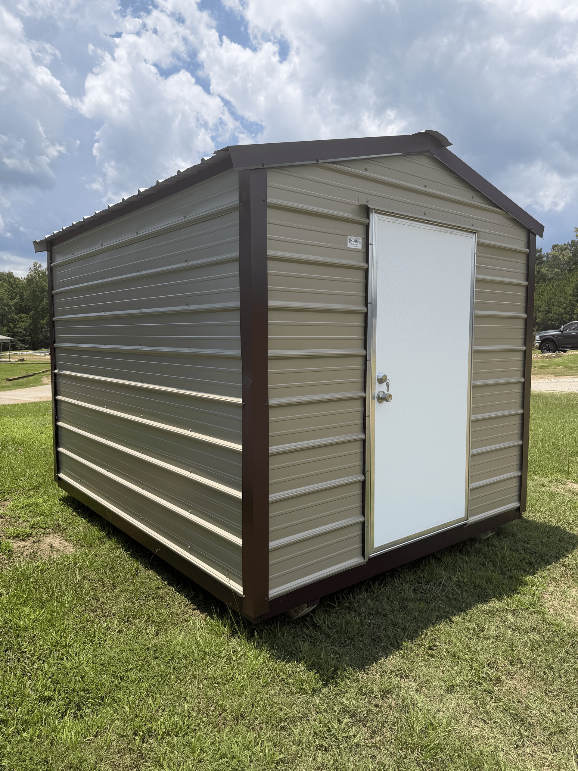 Small beige metal storage shed with a white door on a grassy lawn under a cloudy sky