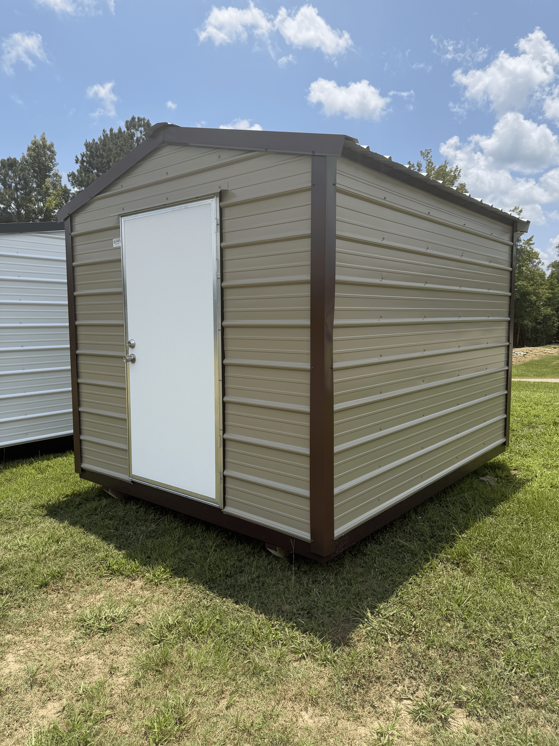 Small beige metal storage shed with white door on grass under a blue sky