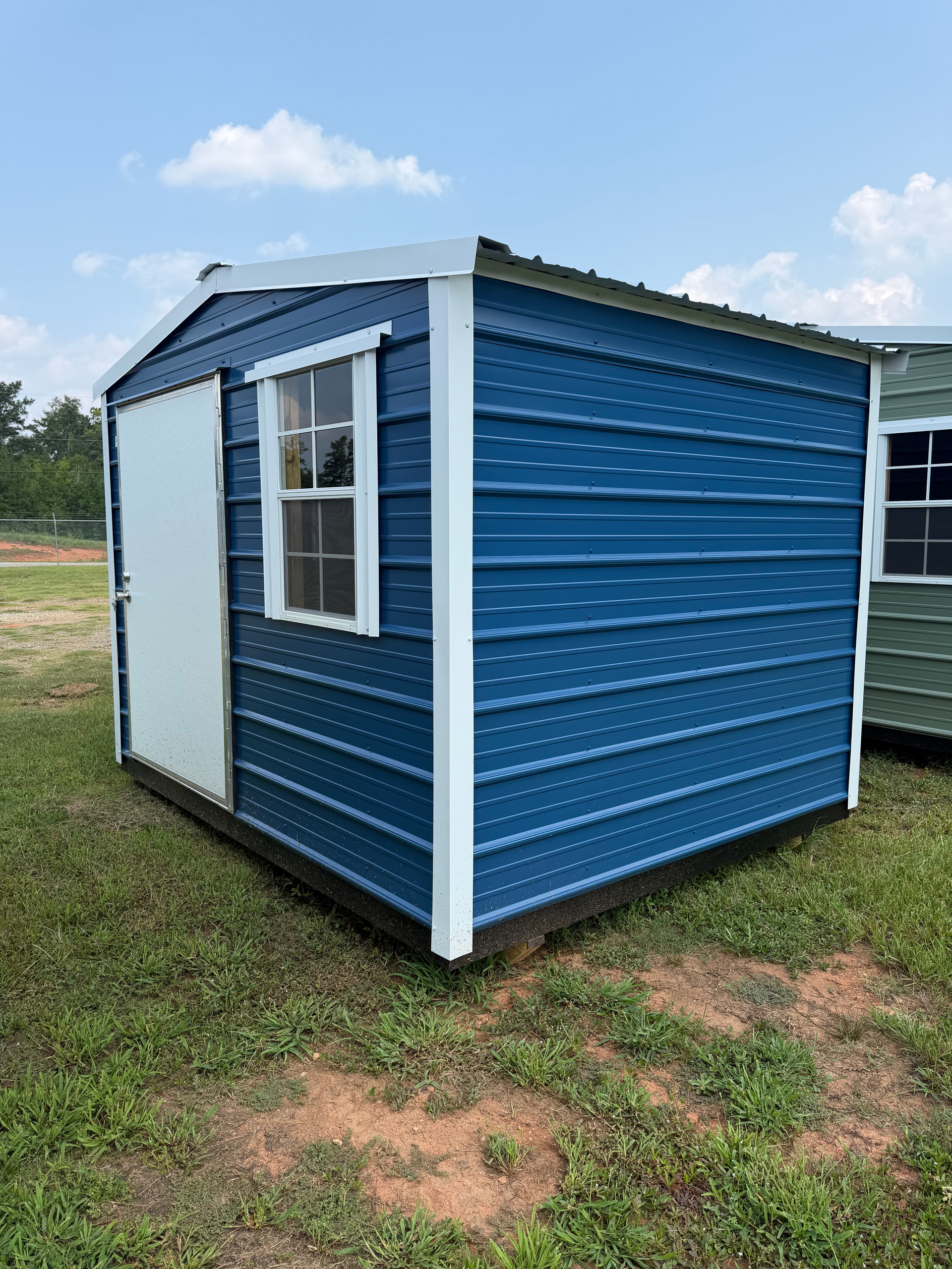 Small blue-and-white shed with windows on a grassy field under a partly cloudy sky