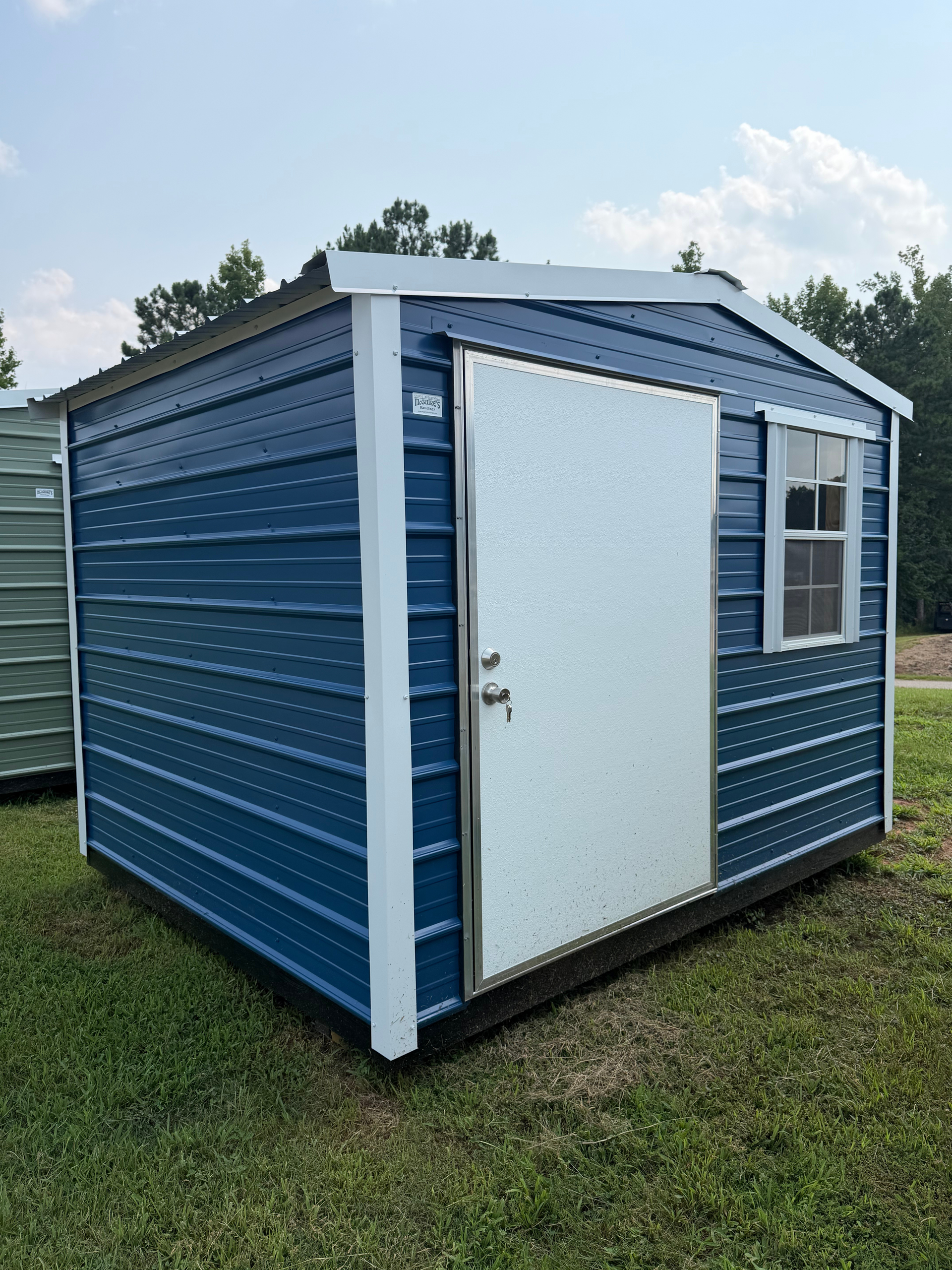 Blue portable storage shed with a white door and window, sitting on grass outdoors.