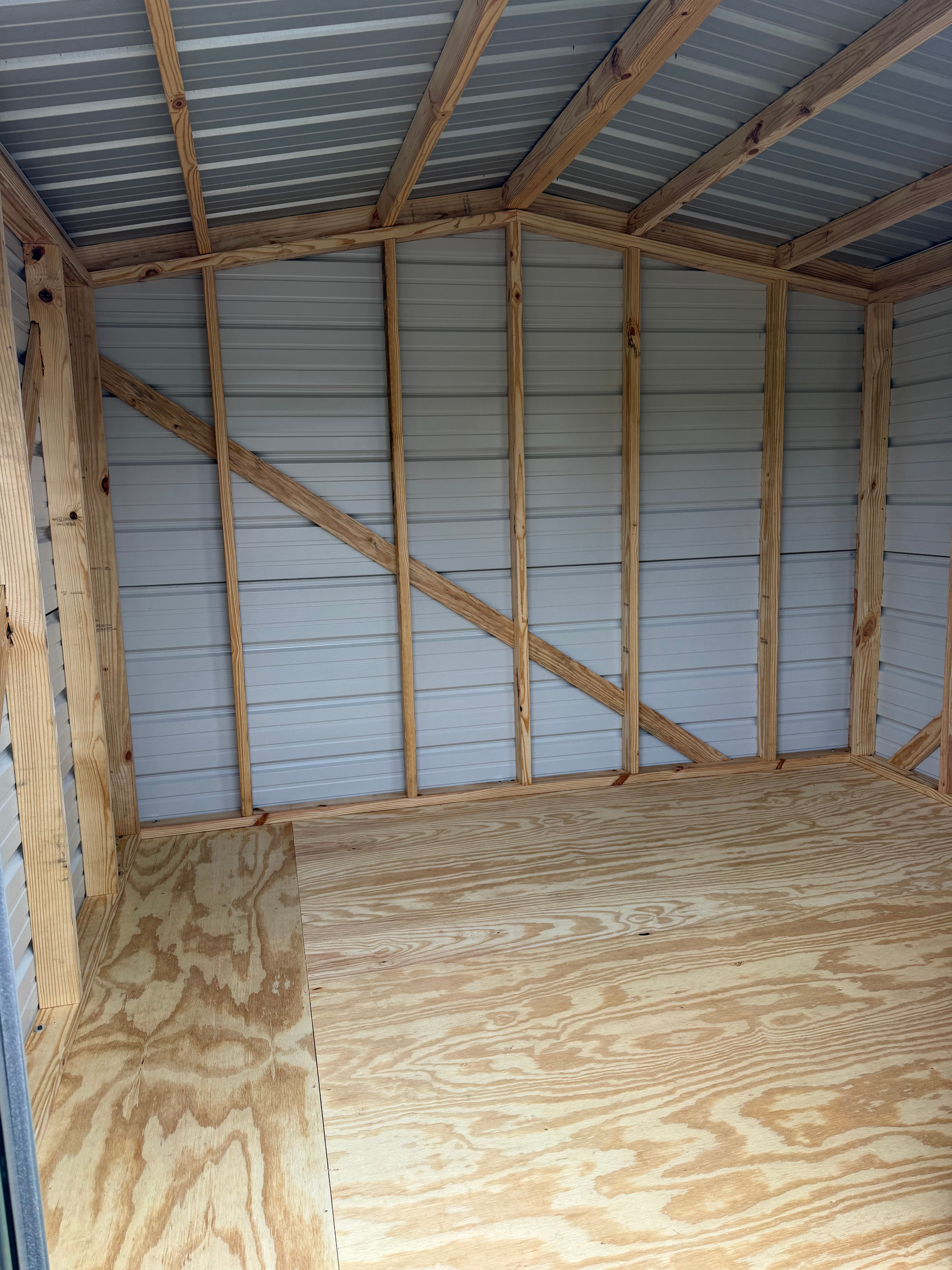 Empty plywood shed interior with exposed wood framing and metal roof panels