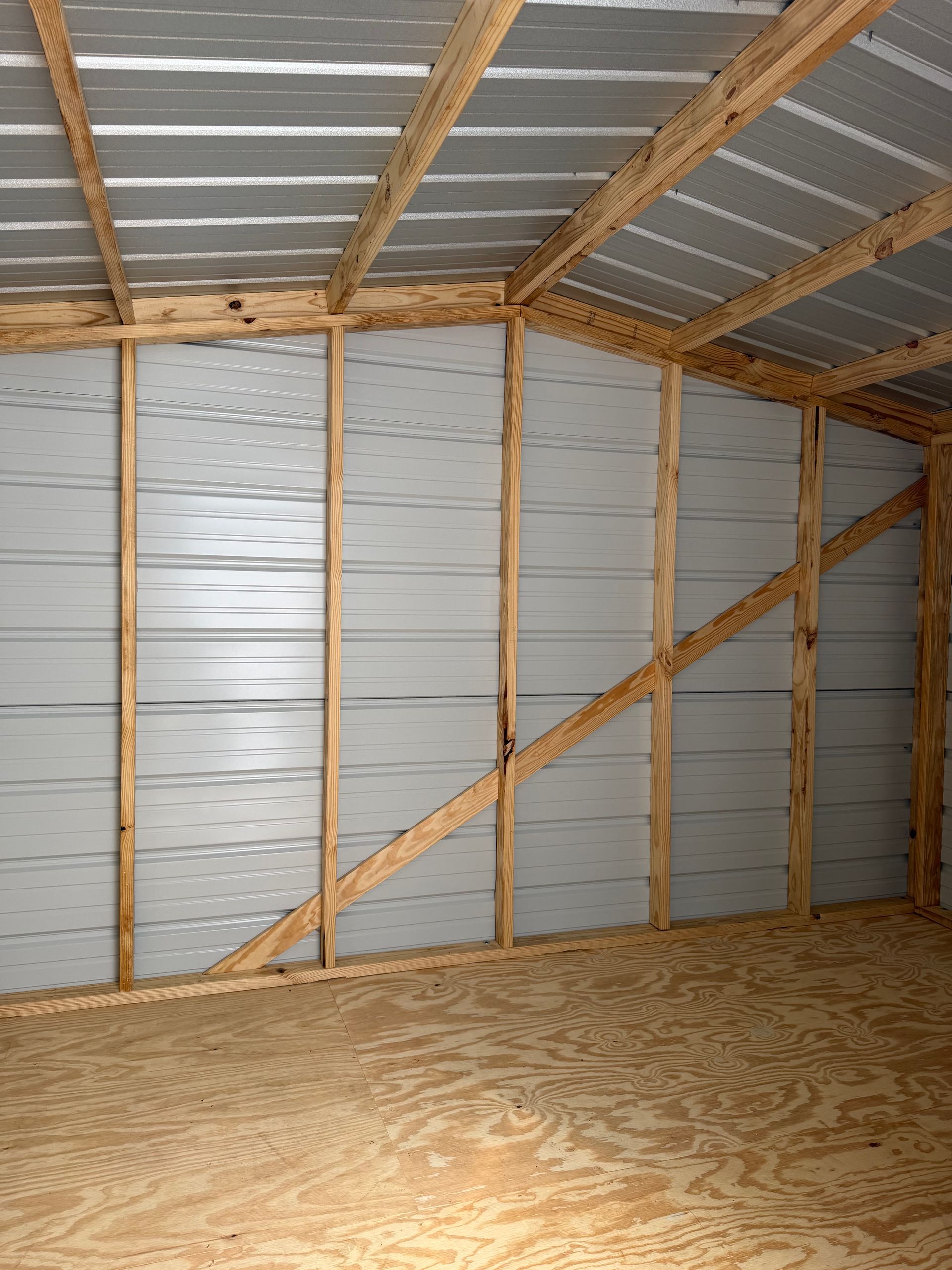 Inside a small shed with plywood floor, metal walls, and exposed wood framing on the ceiling and walls.