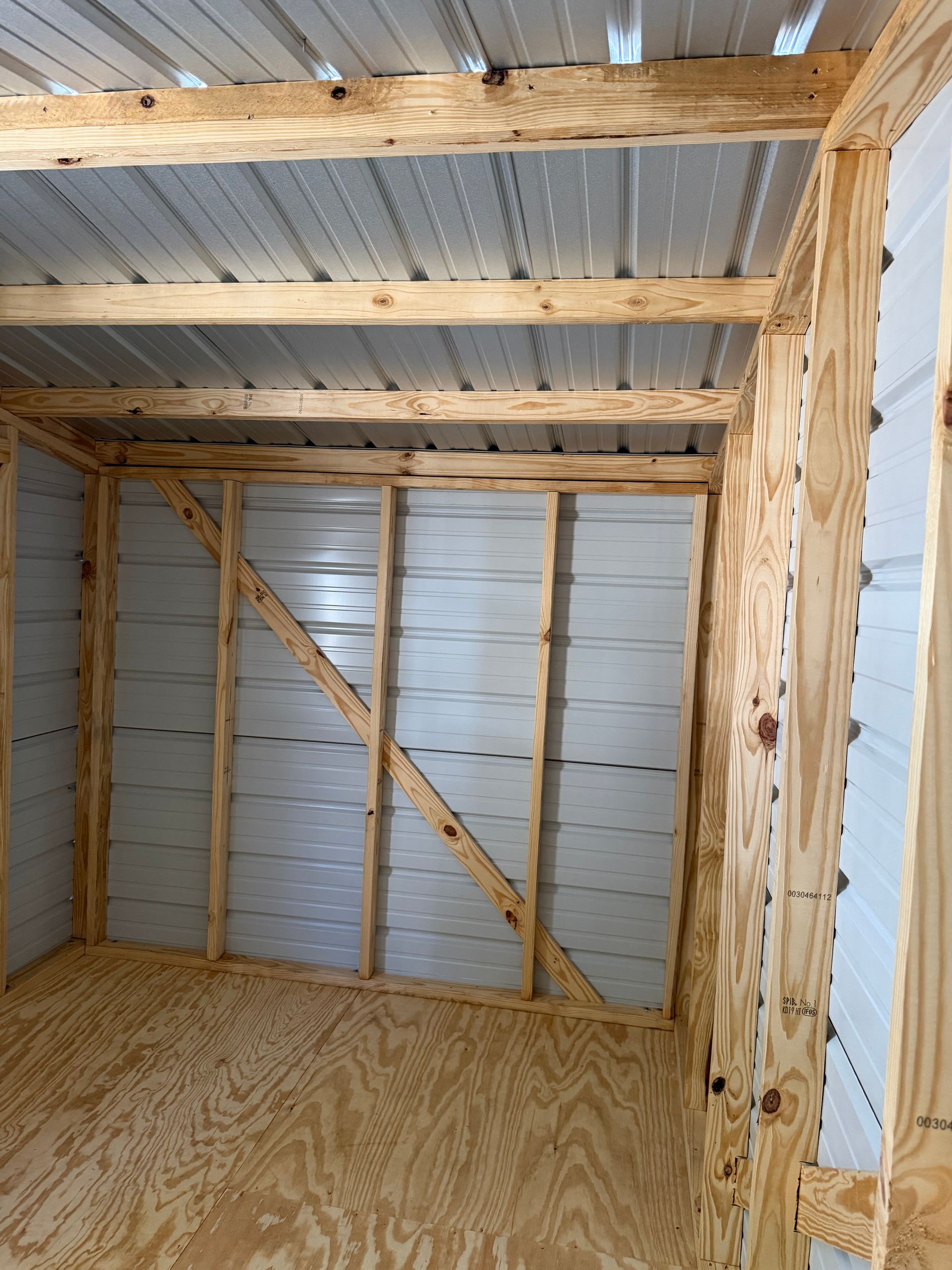 Empty wooden shed interior with unfinished plywood floor, exposed studs, and corrugated metal walls and ceiling