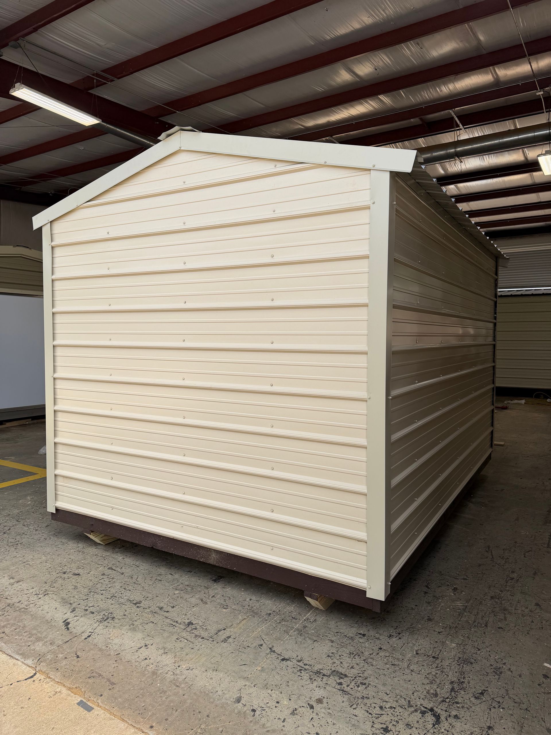 Beige storage shed with pitched roof inside a covered warehouse area.