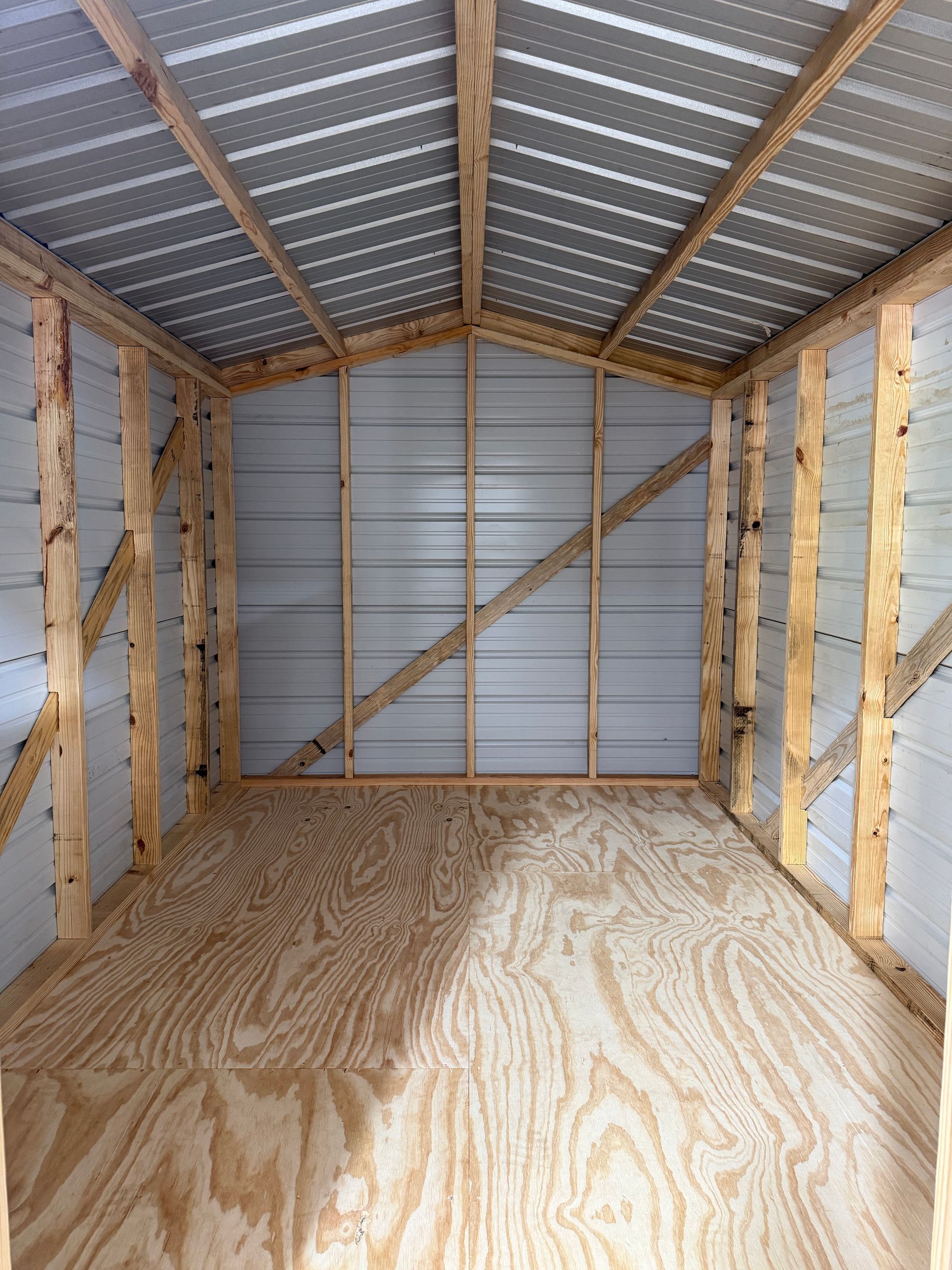 Empty unfinished shed interior with plywood floor, metal roof, and insulated walls