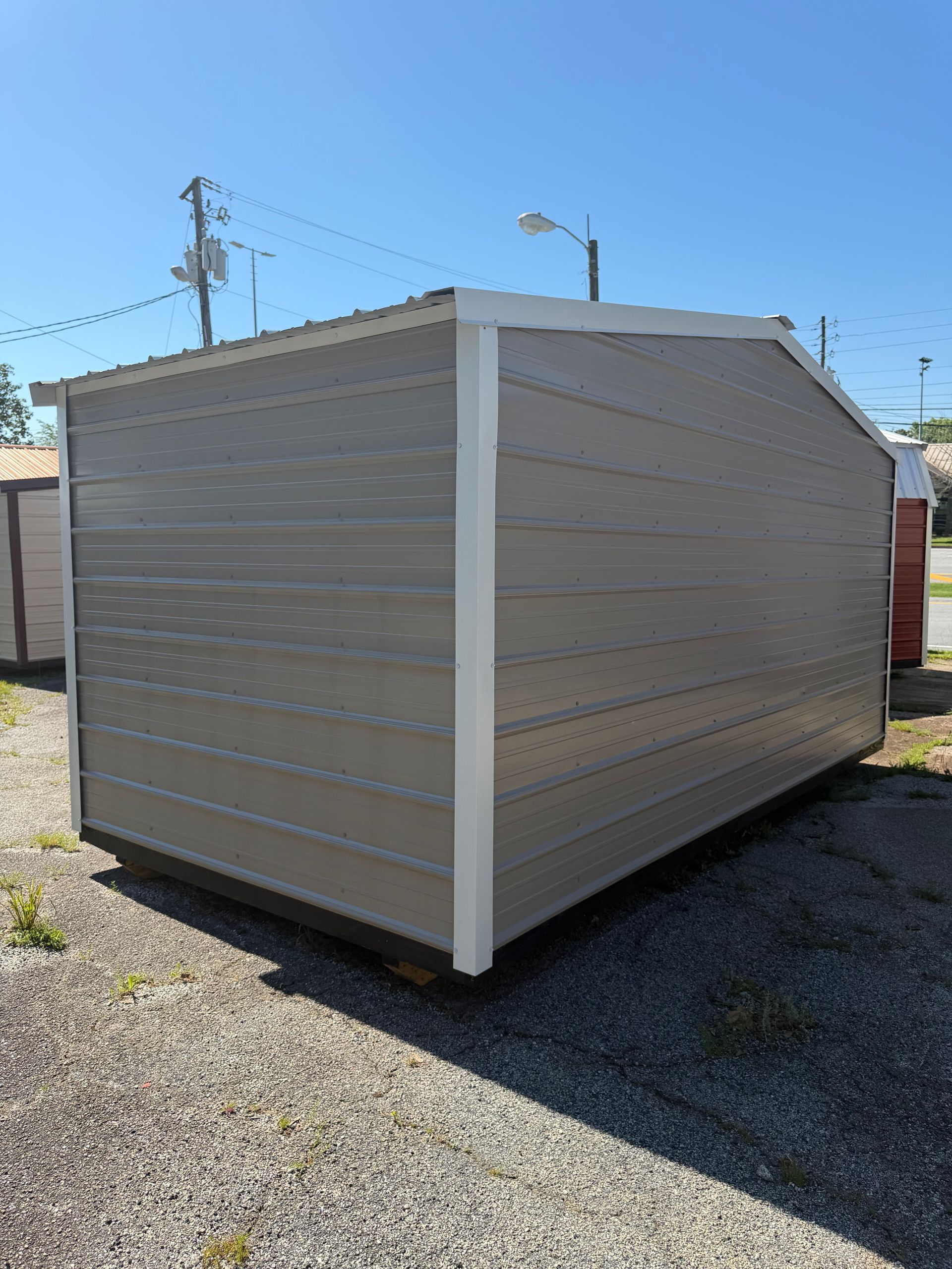 Beige storage shed with white trim on a gravel lot under a clear blue sky