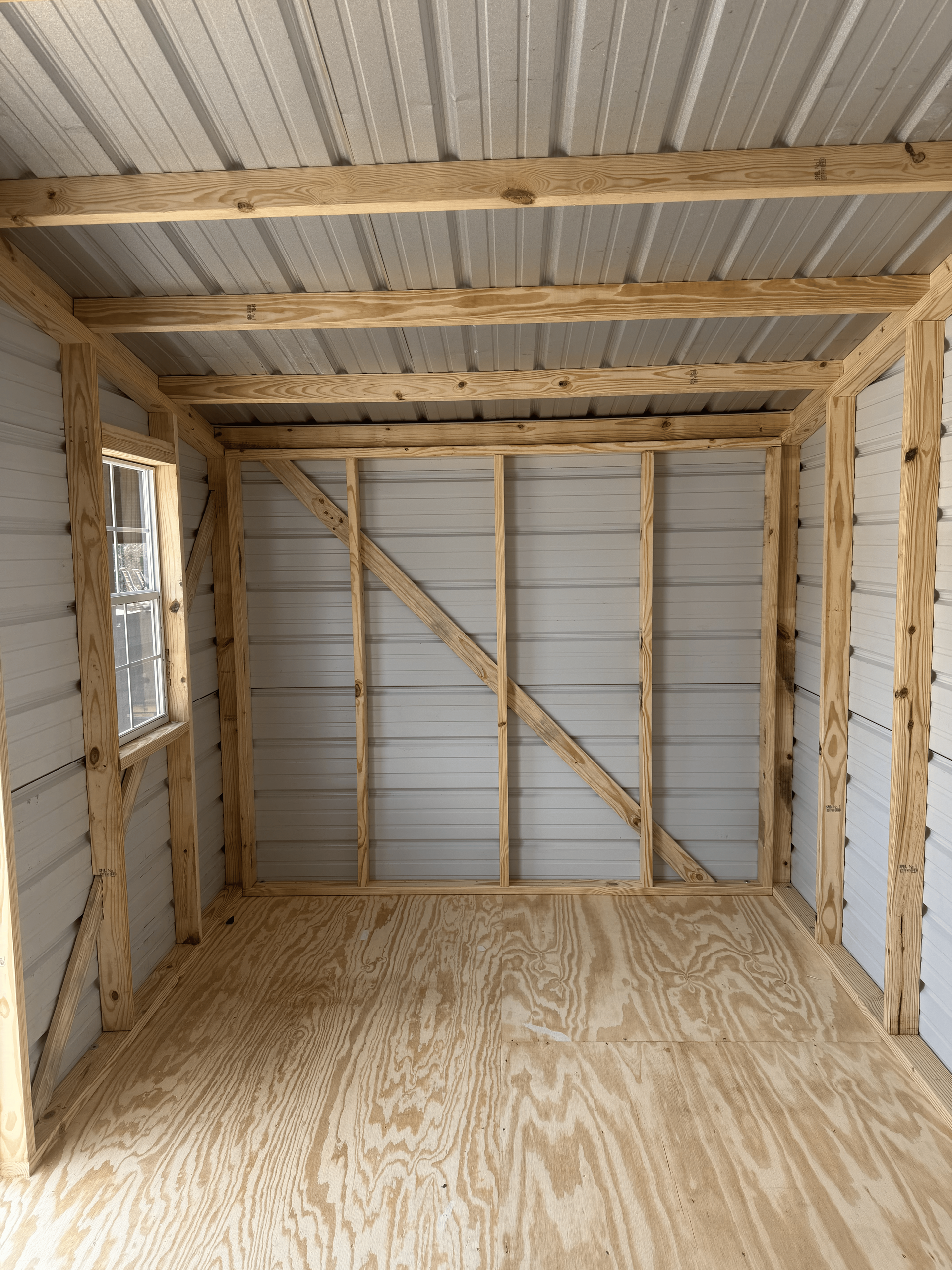 Interior of a small unfinished shed with exposed wooden framing, plywood floor, and metal walls and roof.