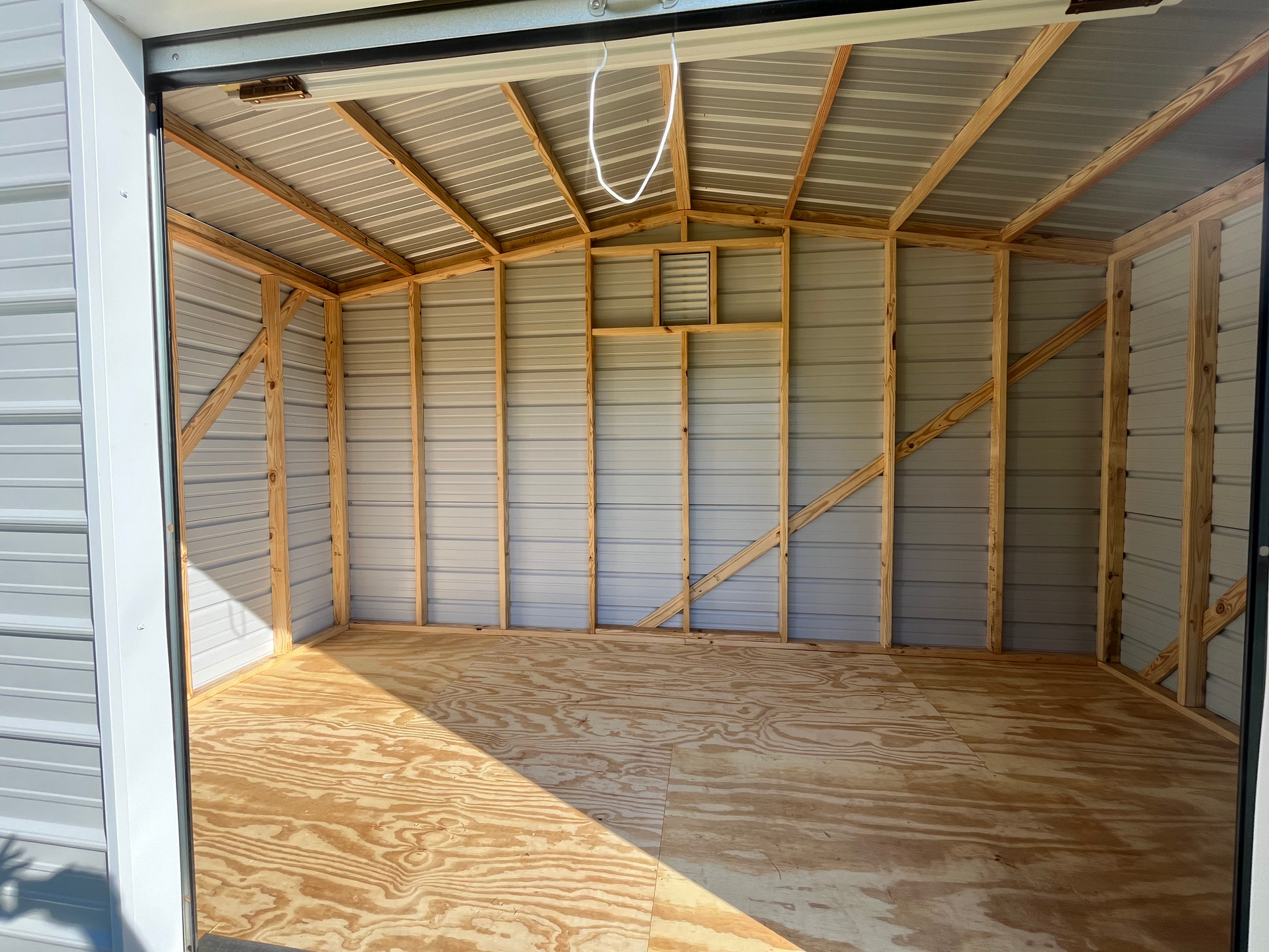 Empty unfinished garage interior with exposed wooden framing and plywood floor, lit by sunlight
