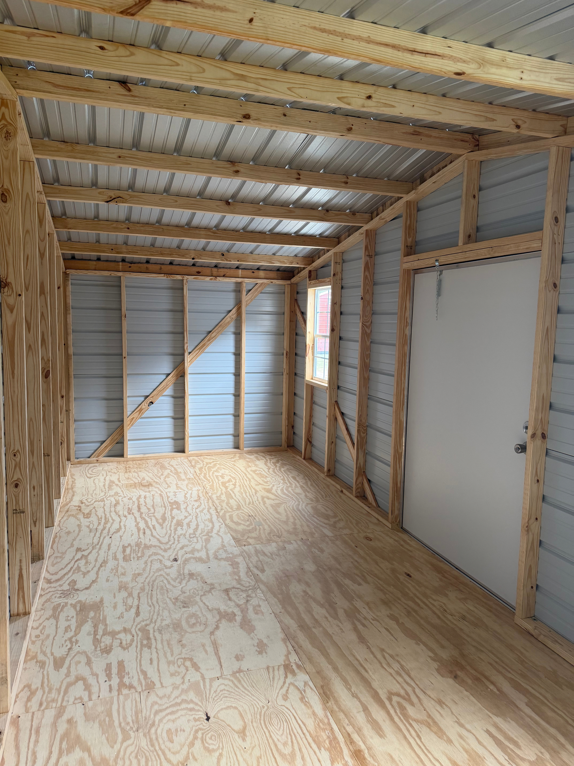 Unfinished interior with plywood floor, exposed studs, and corrugated metal walls and ceiling.