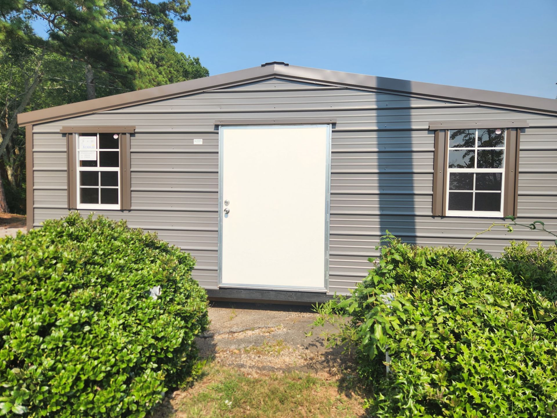 Small beige house with a white front door and windows, partially hidden by green shrubs.