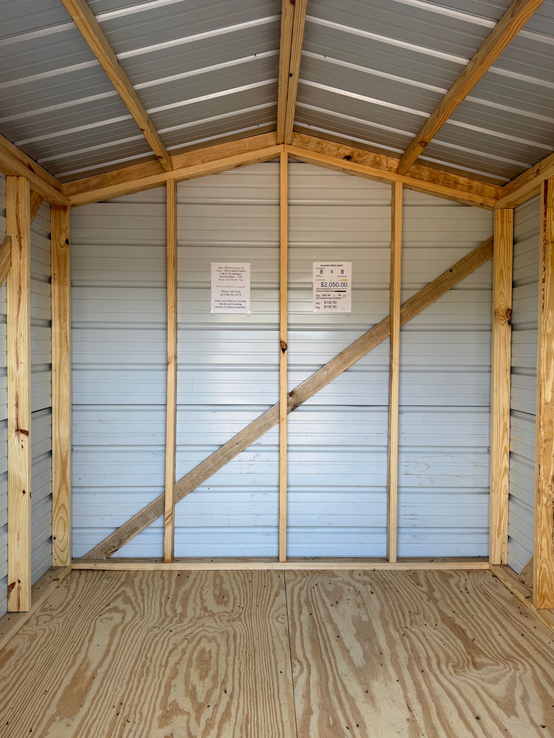 Empty wooden shed with metal walls, diagonal brace, and two safety signs on the back wall